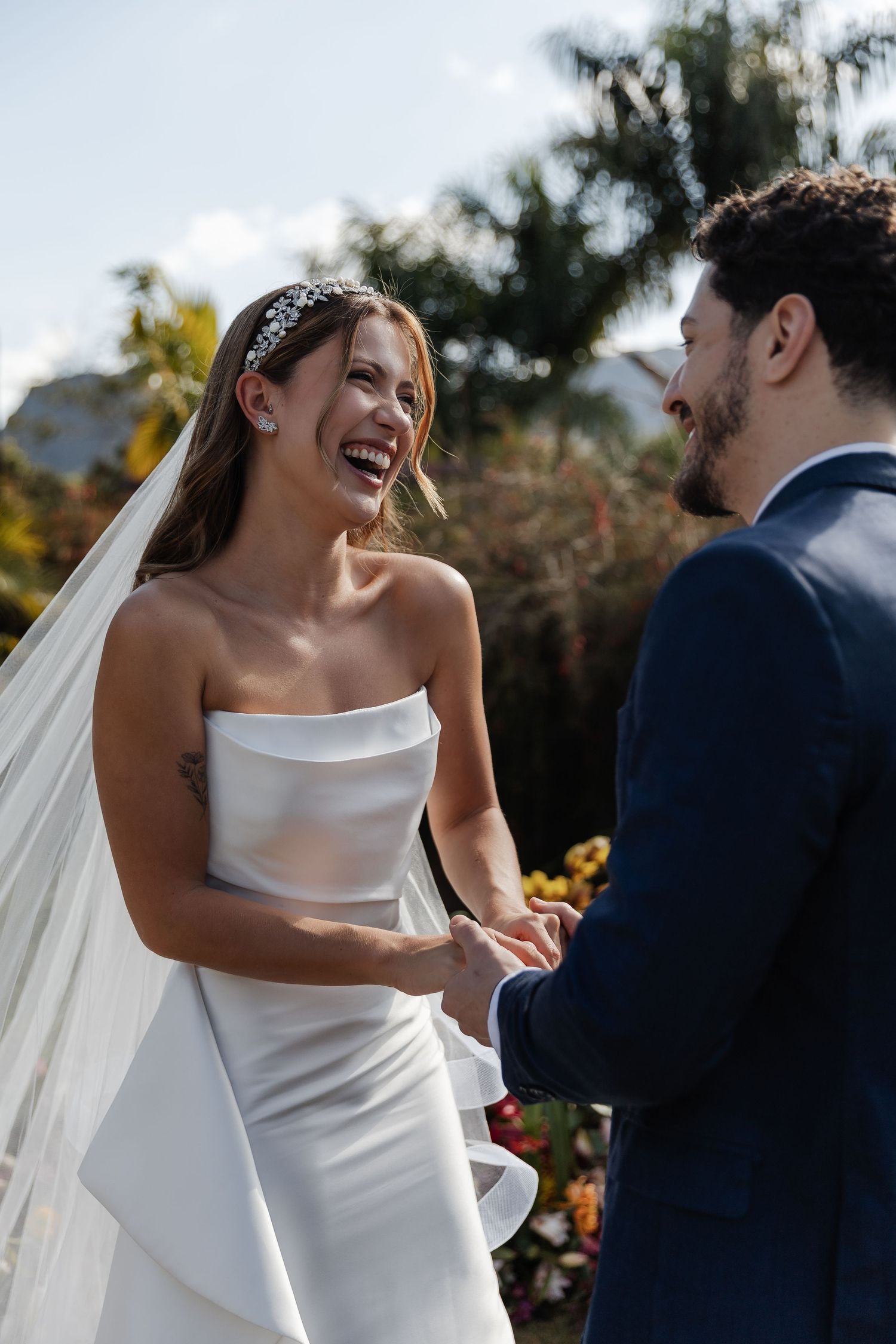 Joyful couple shares a candid moment during their outdoor wedding ceremony, bride wearing an elegant white strapless gown.