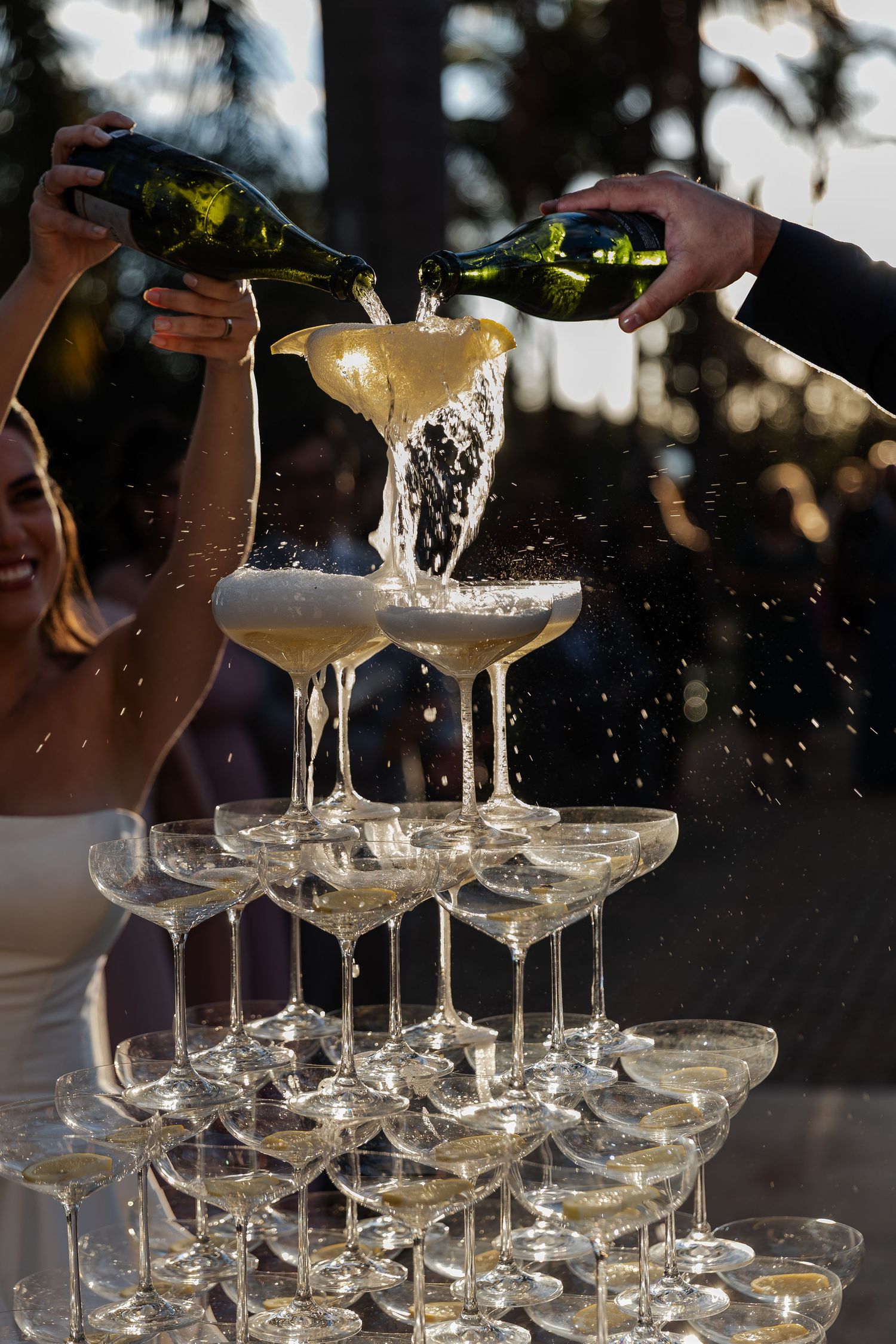 Champagne being poured into a tower of stacked coupe glasses creating an elegant cascade effect at dusk.