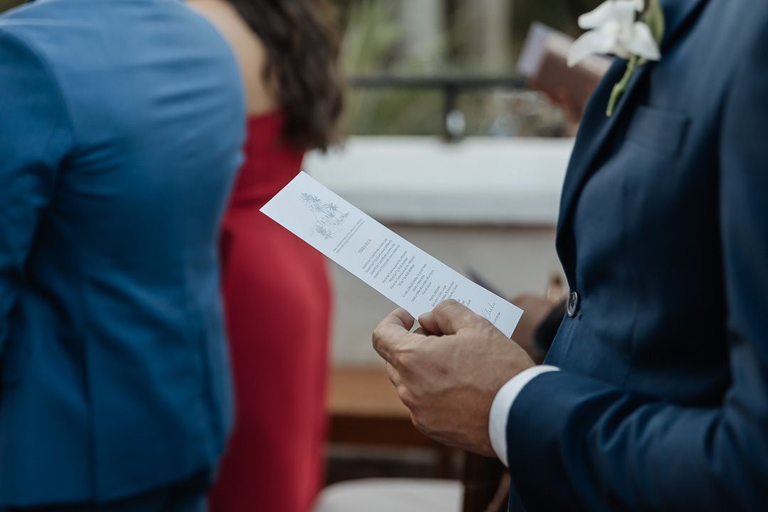 A person in a suit holds a paper during what appears to be a wedding ceremony.