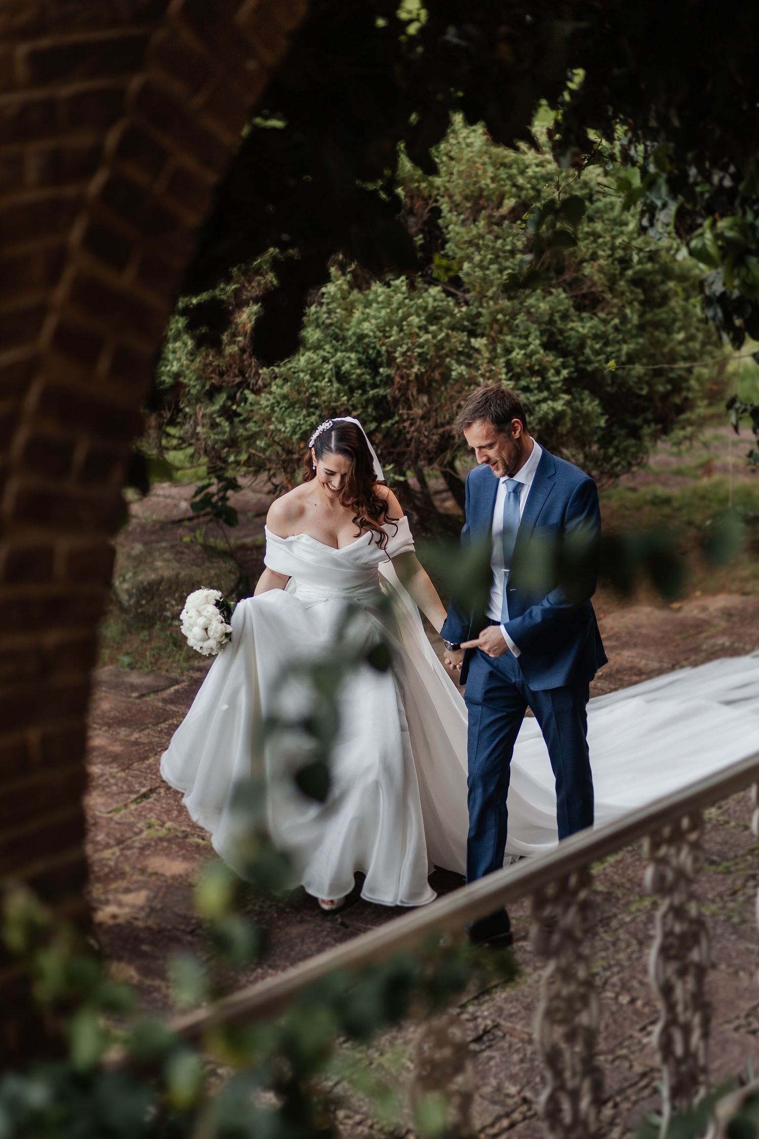 A bride and groom share an intimate moment on a garden path during their wedding photoshoot.