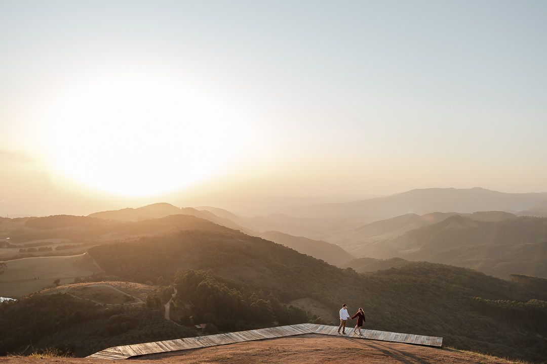 Two silhouettes stand on viewing platform overlooking misty mountain ranges at sunset with golden light.
