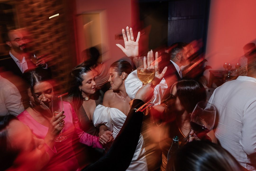 Crowd of people dancing and celebrating at a party with their hands raised under red lighting.