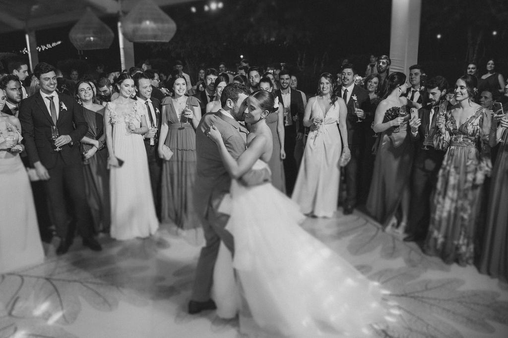 A black and white photo of a couple's first dance at their wedding reception, surrounded by guests watching the moment.