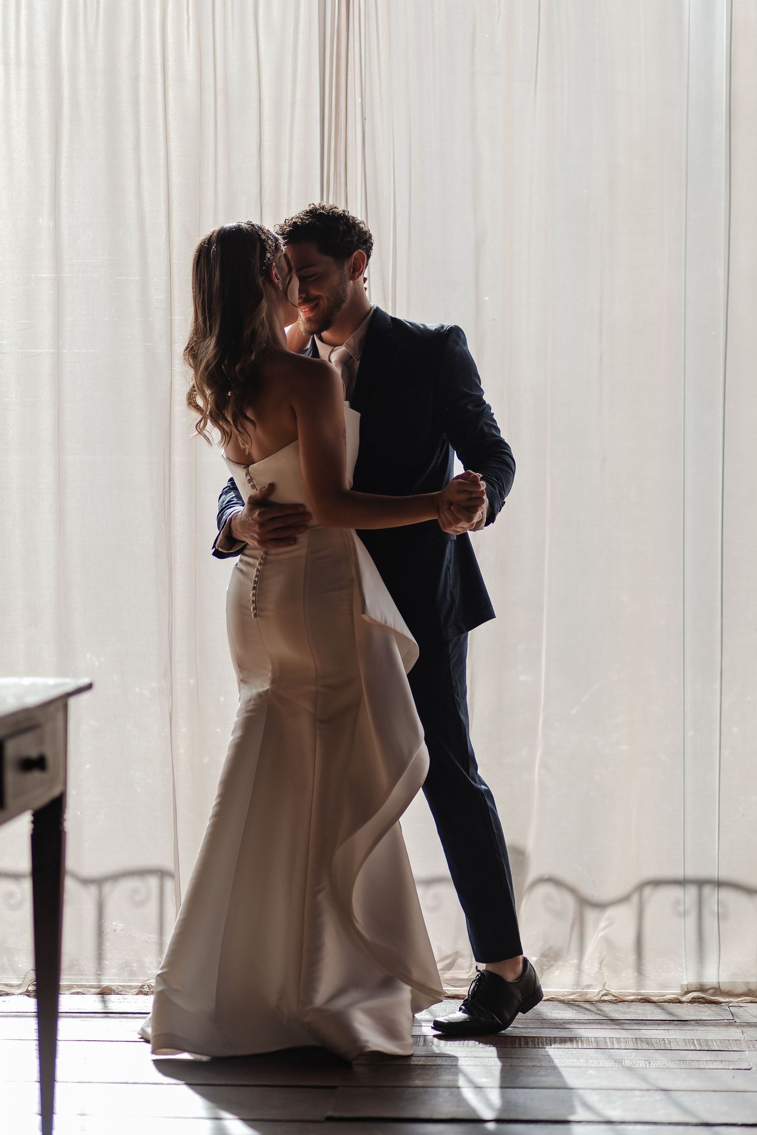 Bride and groom share an intimate dance behind sheer white curtains in a romantic silhouette.