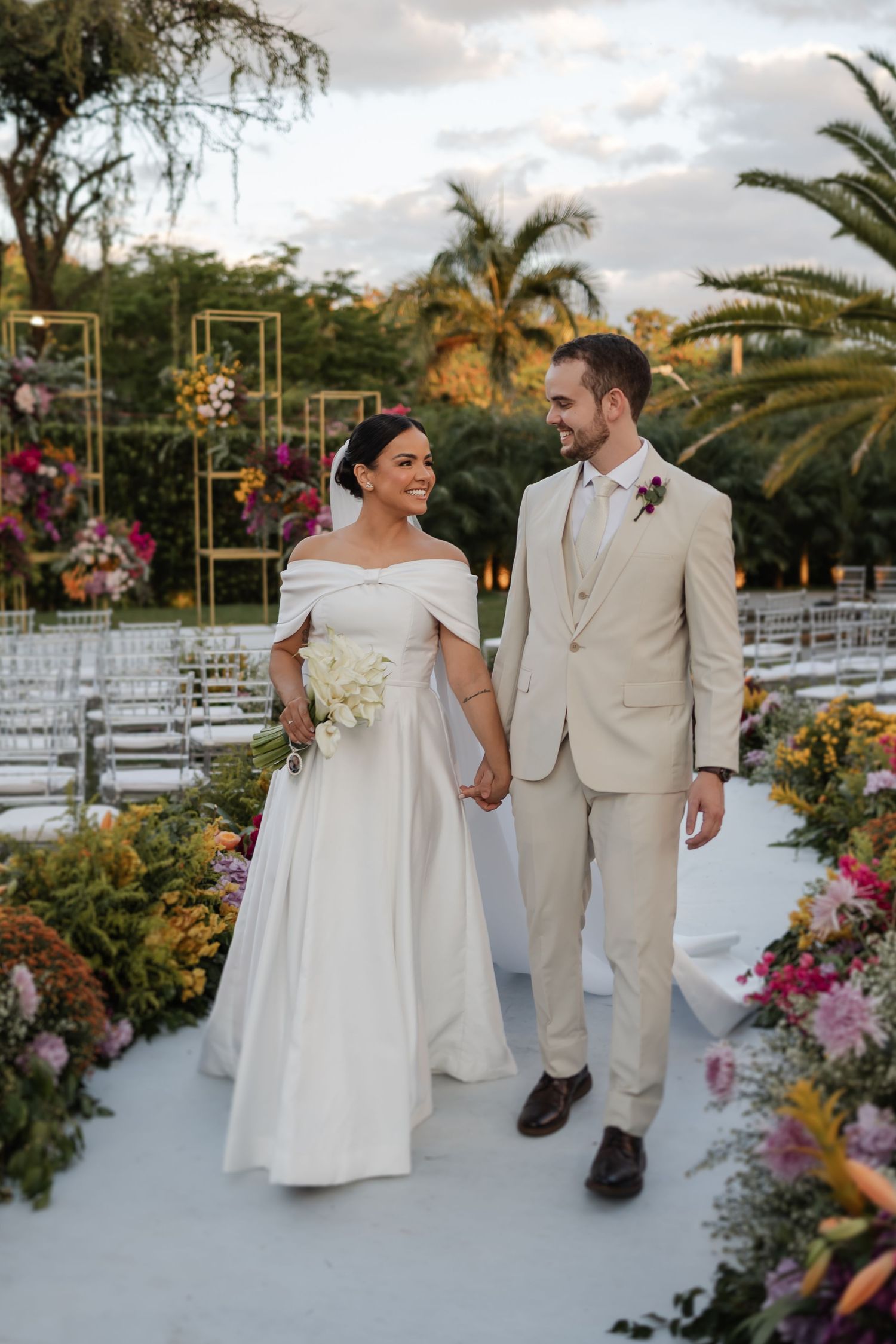 Wedding couple celebrates in an outdoor garden venue with white chairs and tropical palm trees in the background.