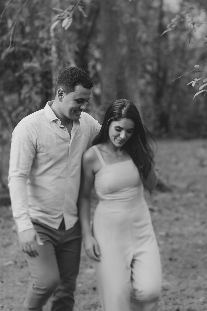 Black and white romantic photo of couple walking together in nature, with her in a jumpsuit and him in casual attire.