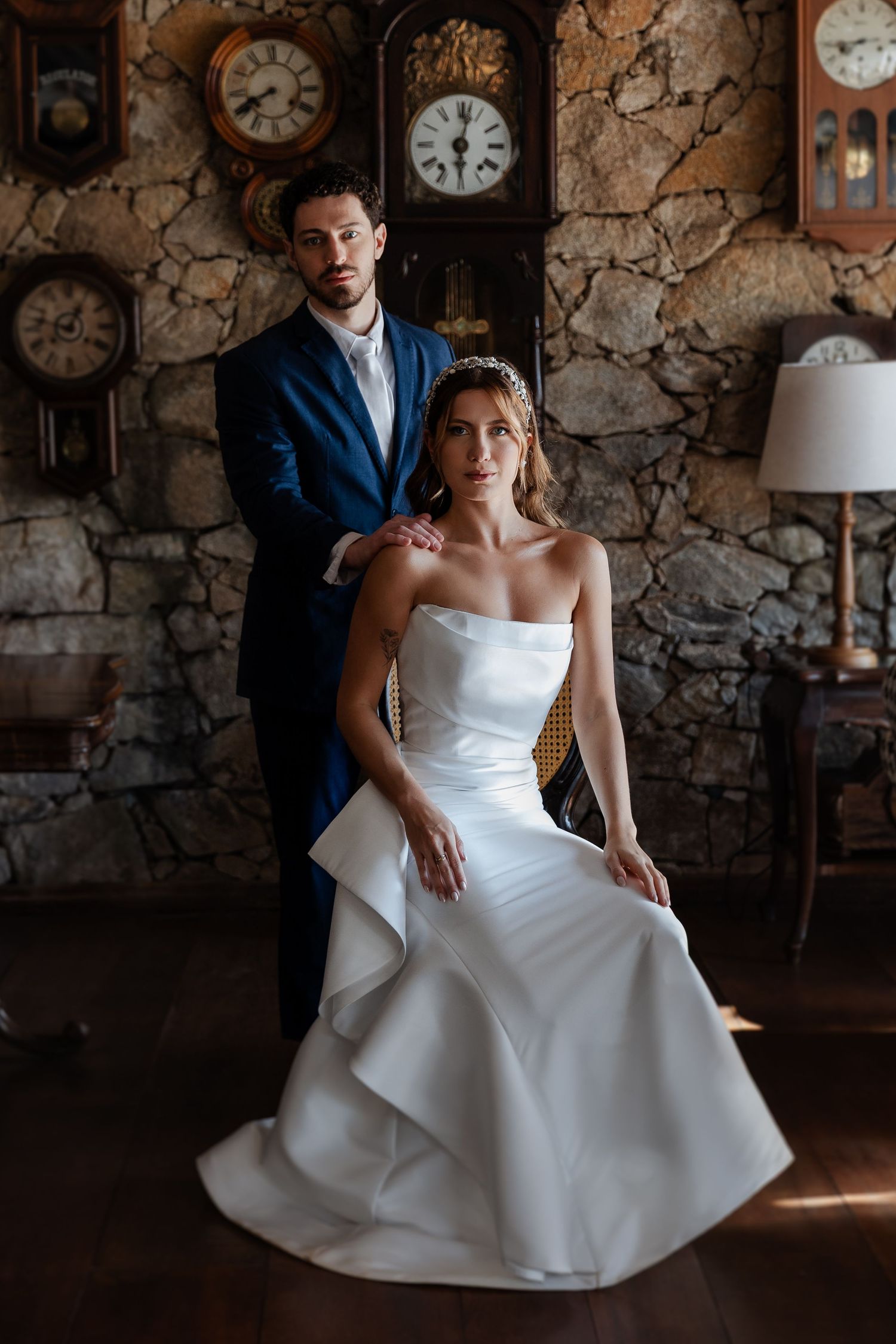 Wedding couple poses in romantic rustic setting with vintage clocks and stone walls in moody lighting.