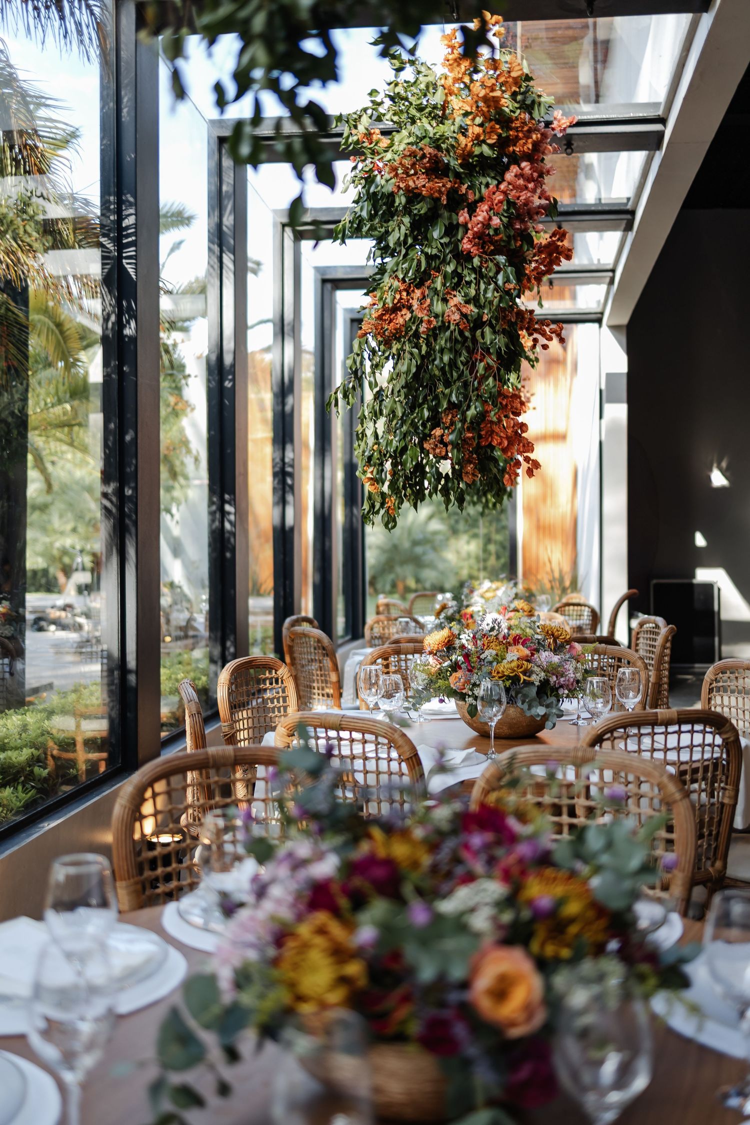 casamento em Belo HorizoWedding reception venue decorated with elegant floral arrangements and rattan chairs in a sunlit conservatory space.