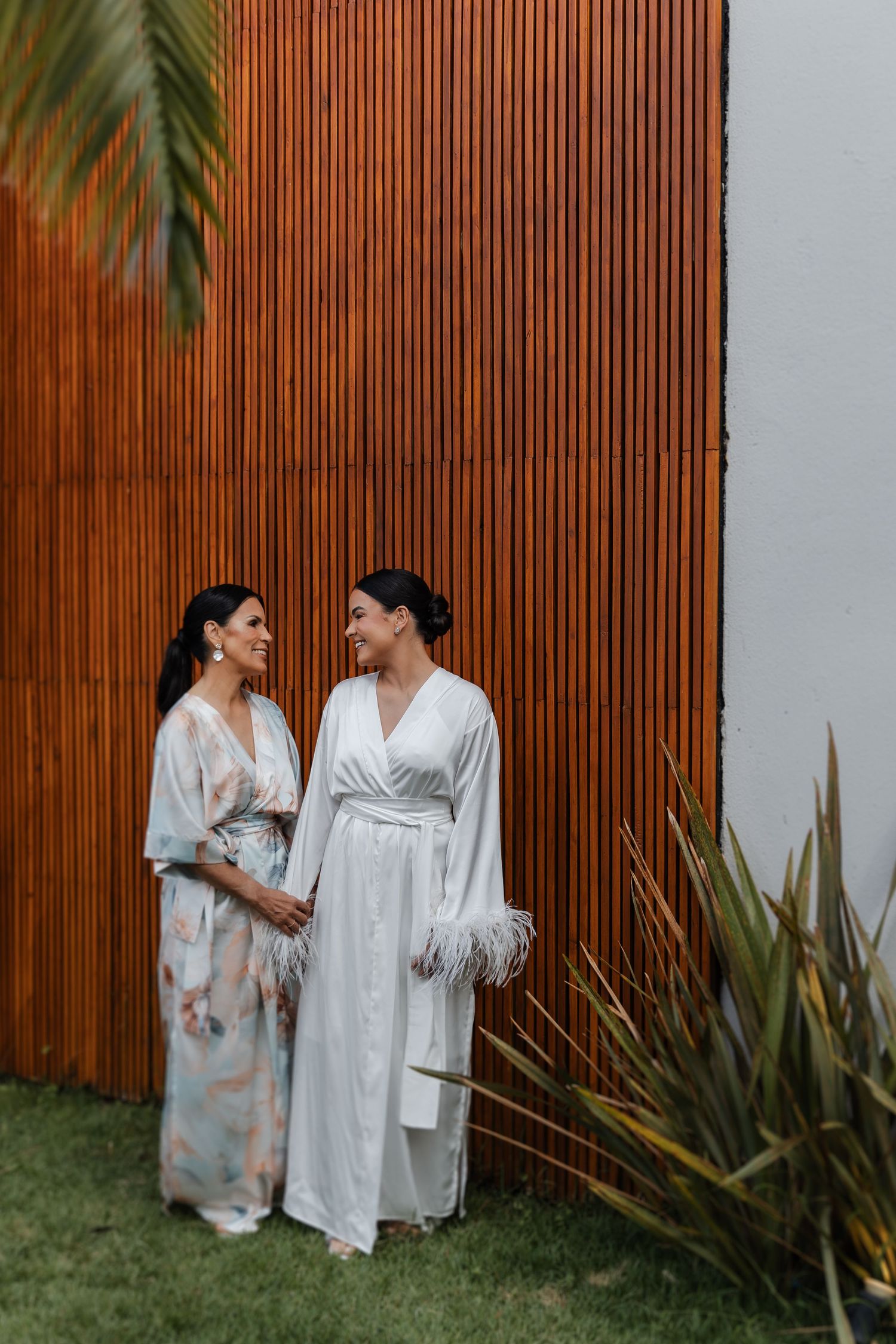 Two people in white robes share a joyful moment together against a wooden fence backdrop.