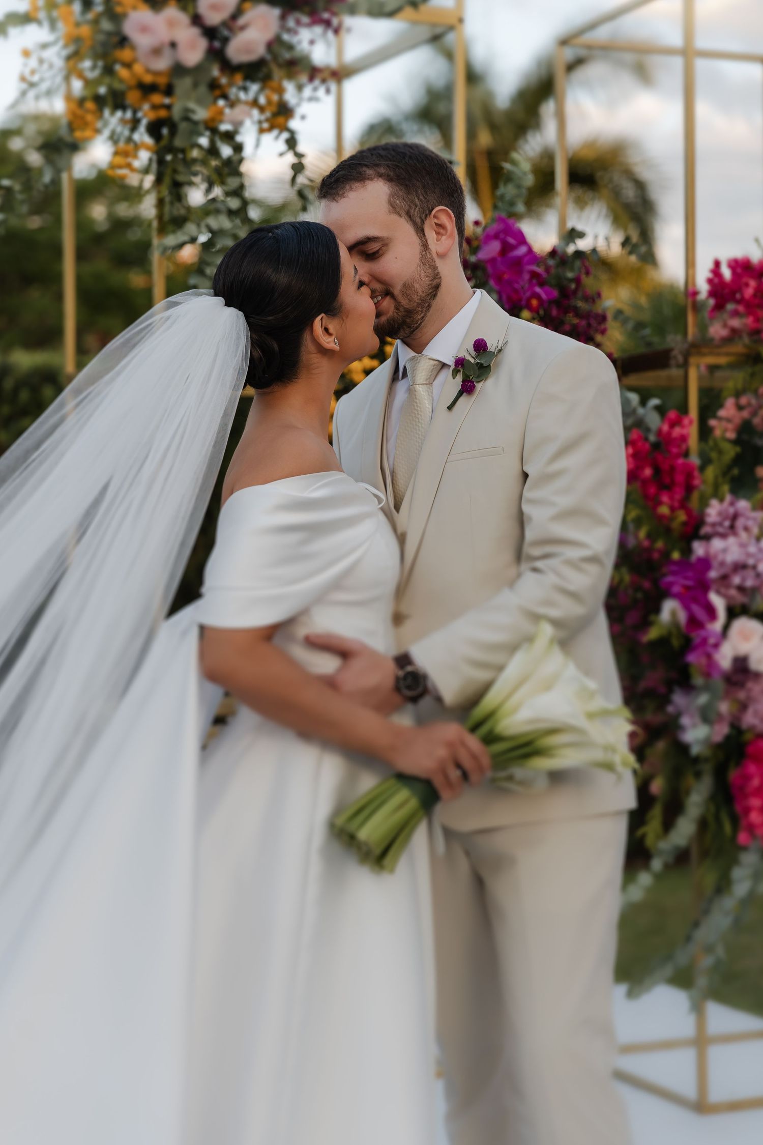 casamento em Belo Horizonte, cA romantic wedding couple embraces under a floral-adorned geometric arch during their outdoor garden ceremony.