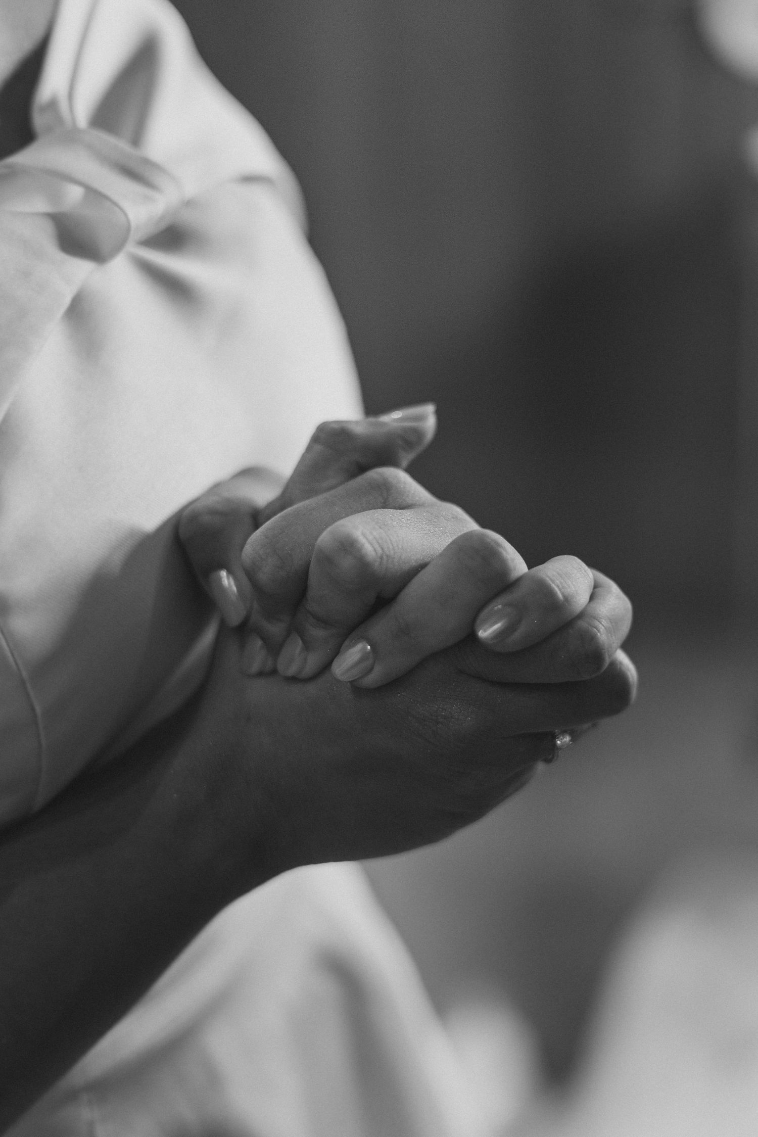 Close-up black and white photograph of hands clasped together in prayer or contemplation against a light background.
