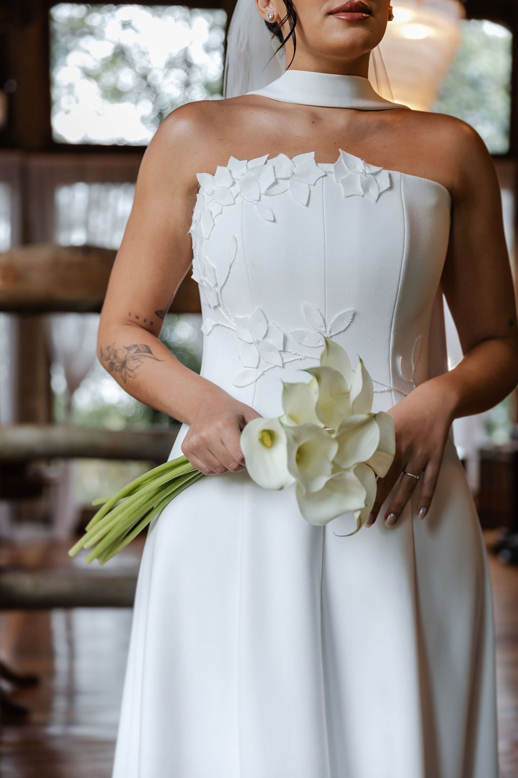 Fotógrafo de casameA bride in a stunning white strapless wedding dress with floral appliques holds an elegant bouquet of white calla lilies.