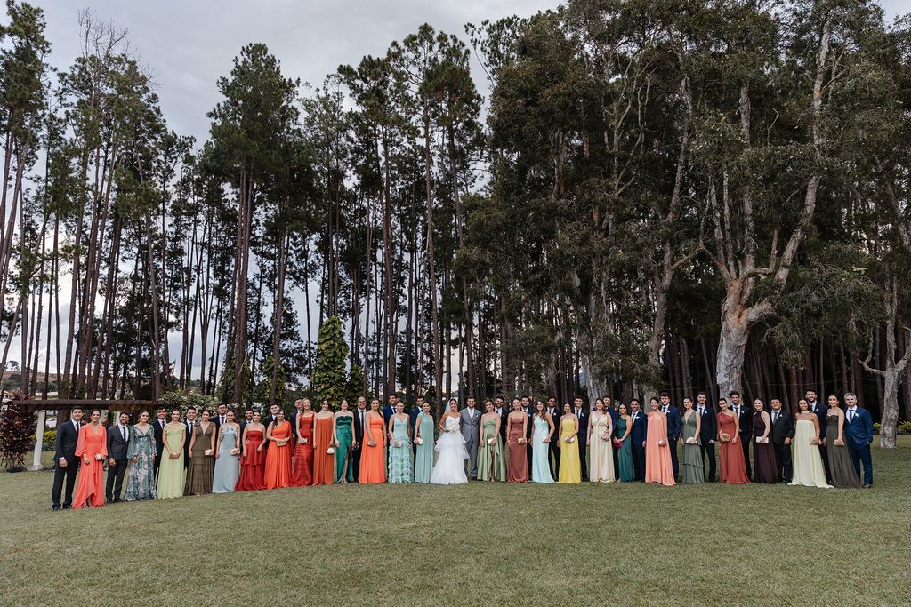 A colorful line of formal dresses stands against a backdrop of tall eucalyptus trees on a grassy lawn.