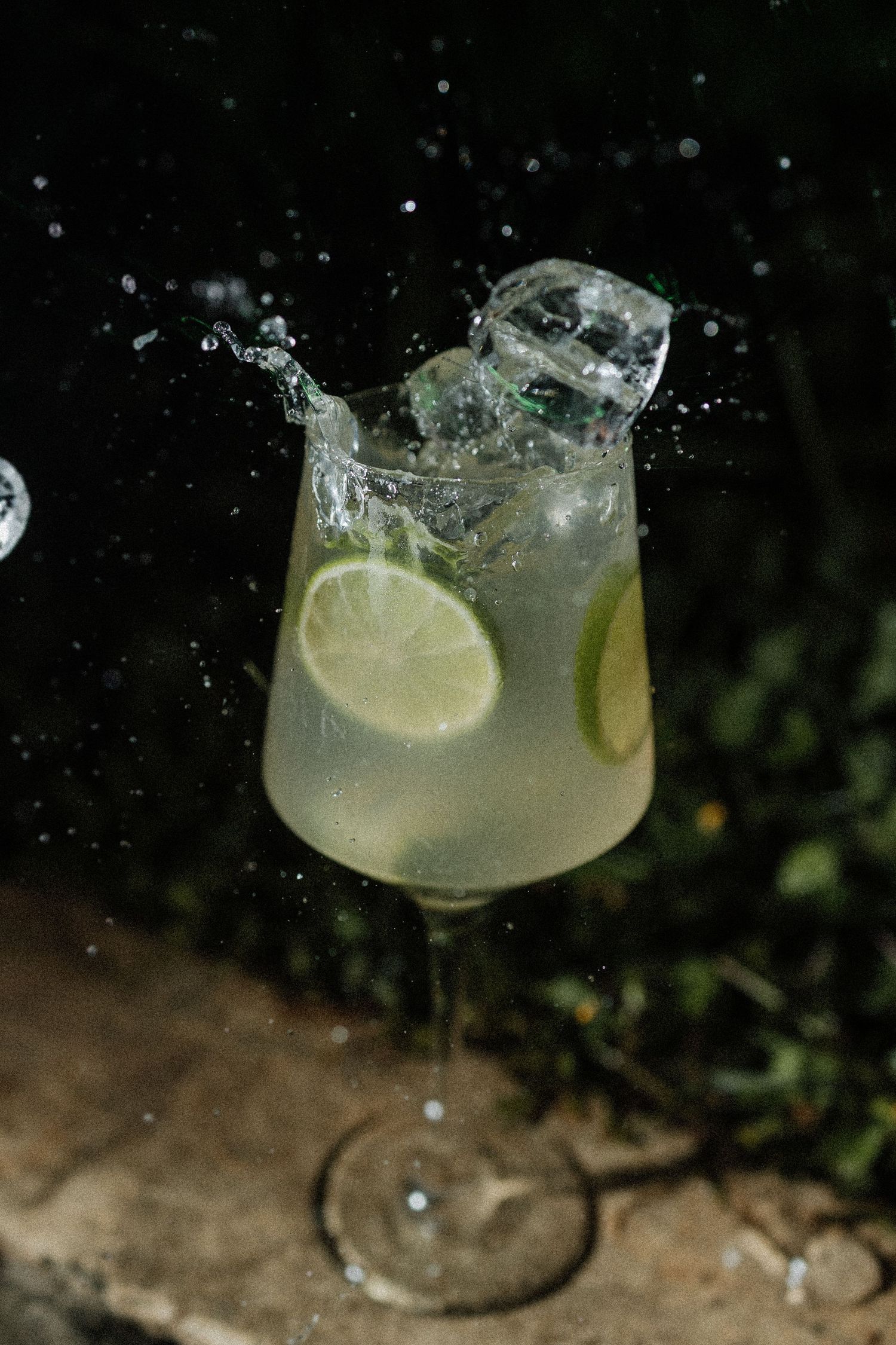 A refreshing glass of lemonade splashing with ice cubes and fresh lemon slices against a dark background.