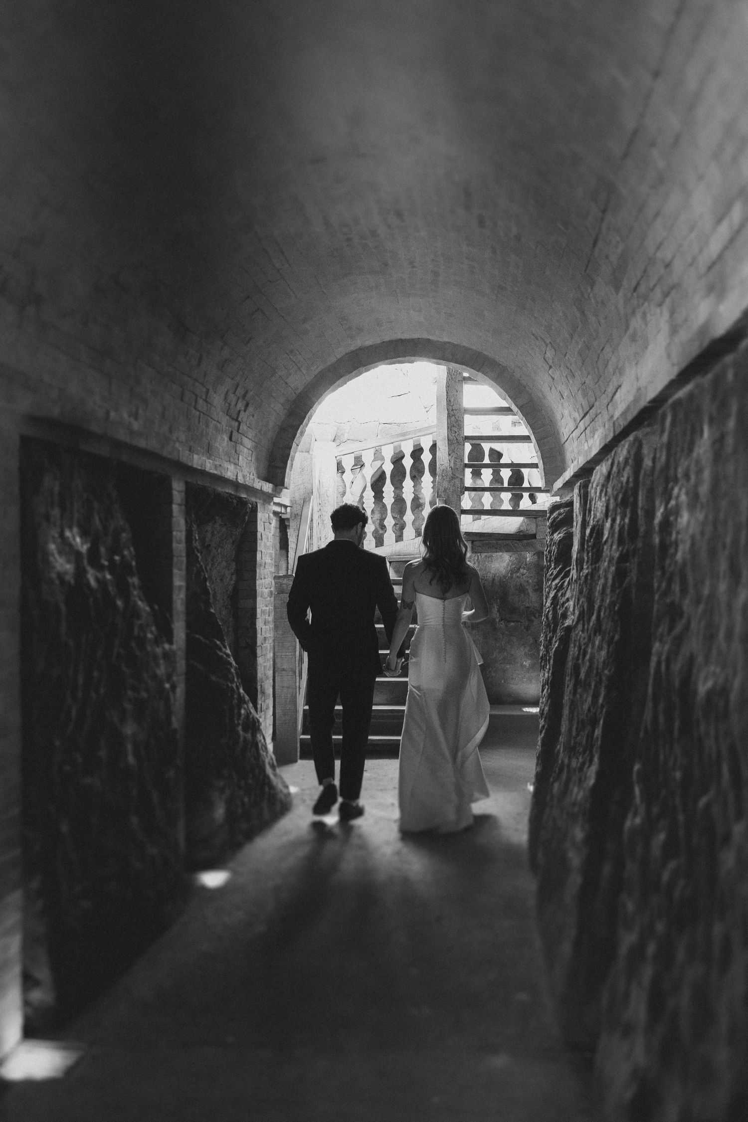 Black and white photography shows silhouetted figures walking through a dark tunnel with arched ceiling and dramatic lighting.