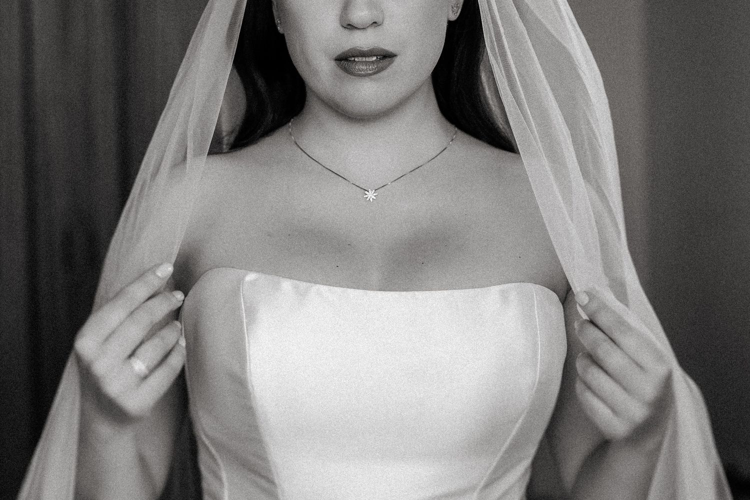 Black and white portrait of a bride wearing a strapless wedding dress and delicate veil with a simple necklace.