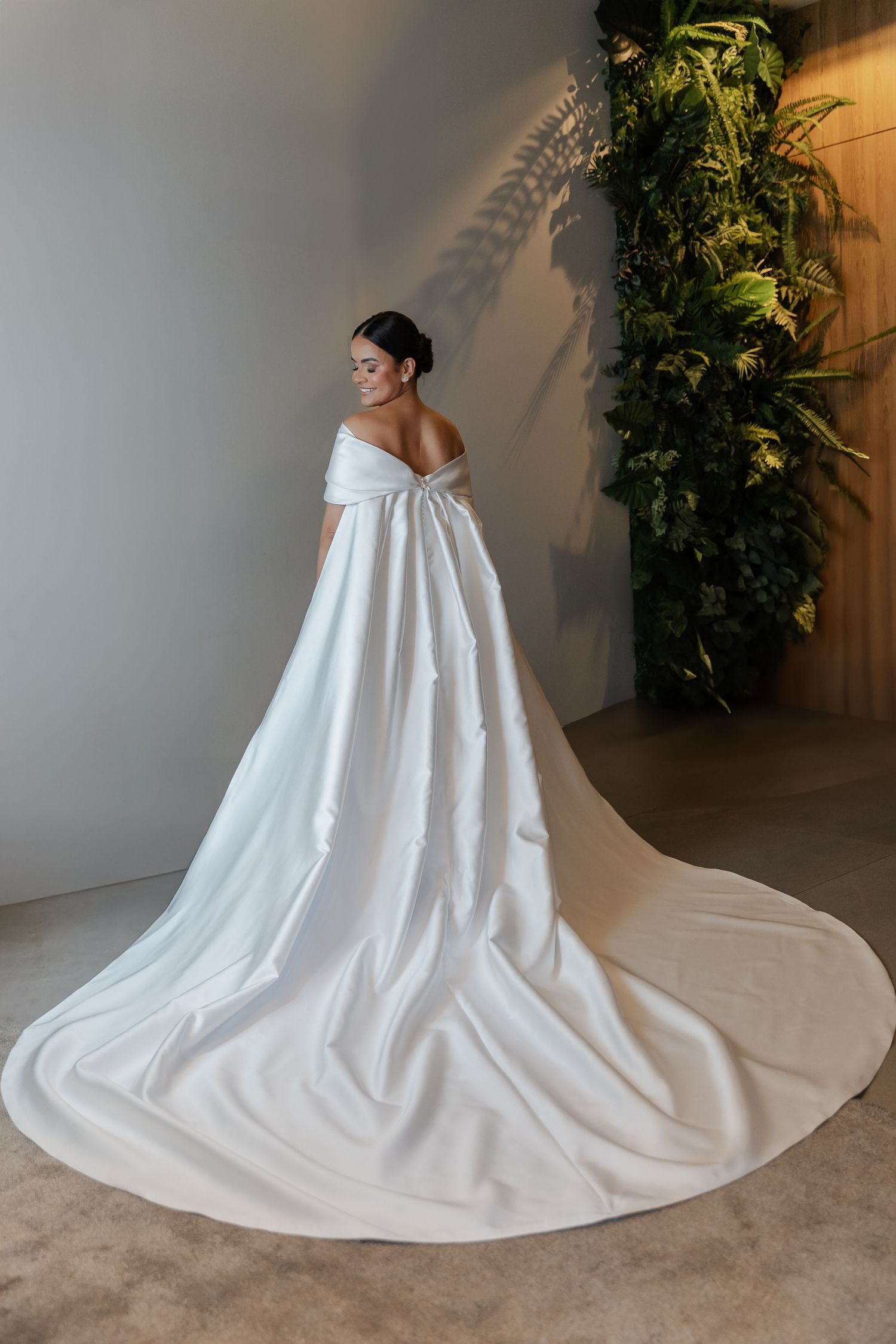 Elegant off-shoulder wedding dress with dramatic cathedral-length train in pure white silk against minimalist backdrop.