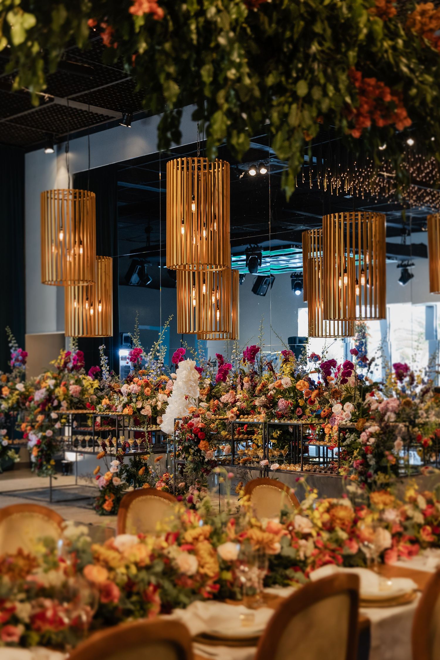 Elegant reception tables adorned with vibrant floral centerpieces and wooden pendant lights hanging from industrial ceiling.