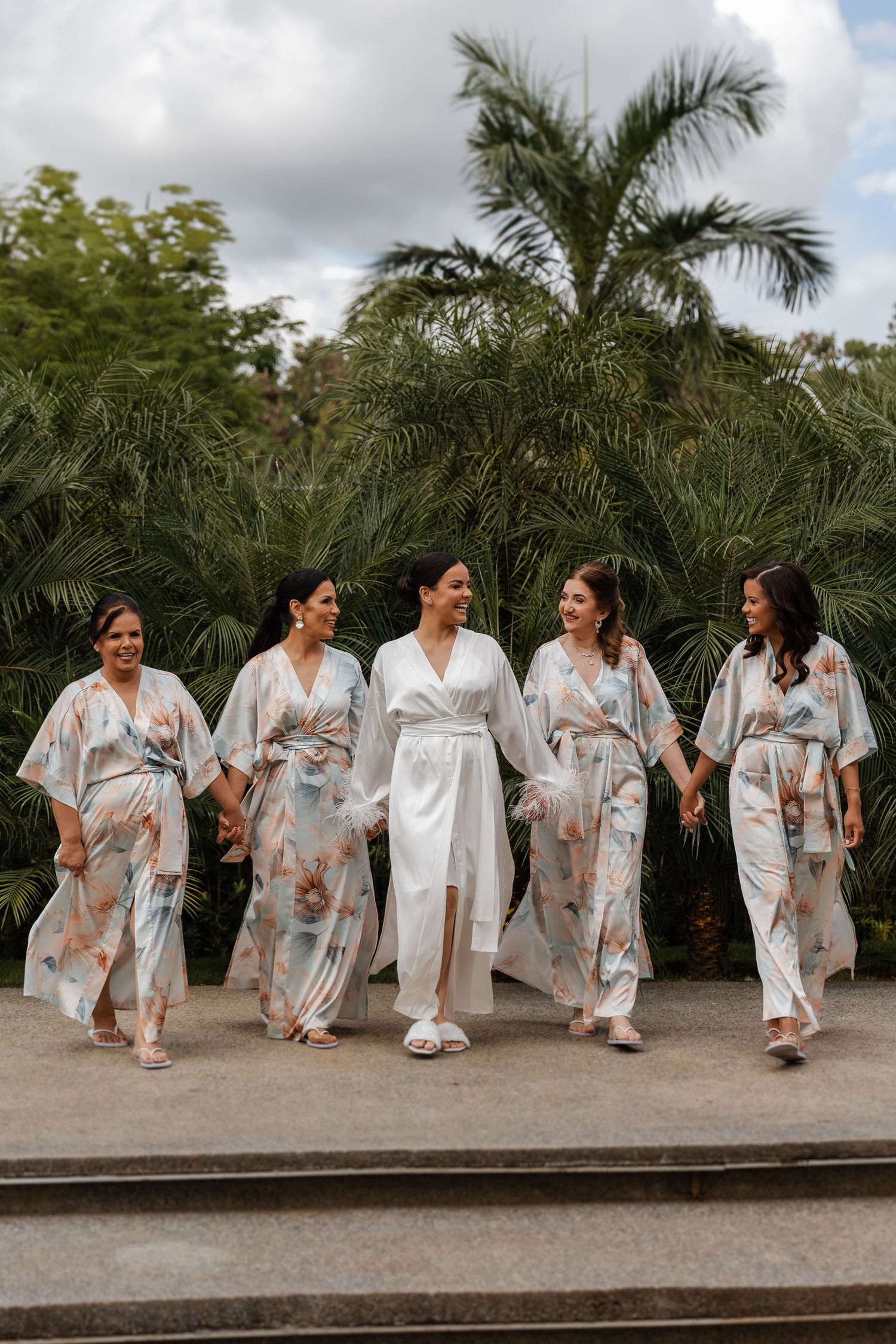 casamento em Belo HorizoA sequence of three photos showing a bridal party wearing matching floral robes sitting together on a concrete wall.