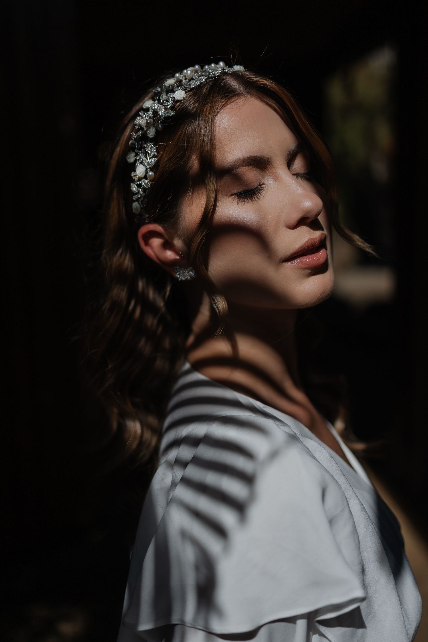 A moody portrait with dramatic shadows shows someone in a striped sweater and floral headpiece looking up pensively.