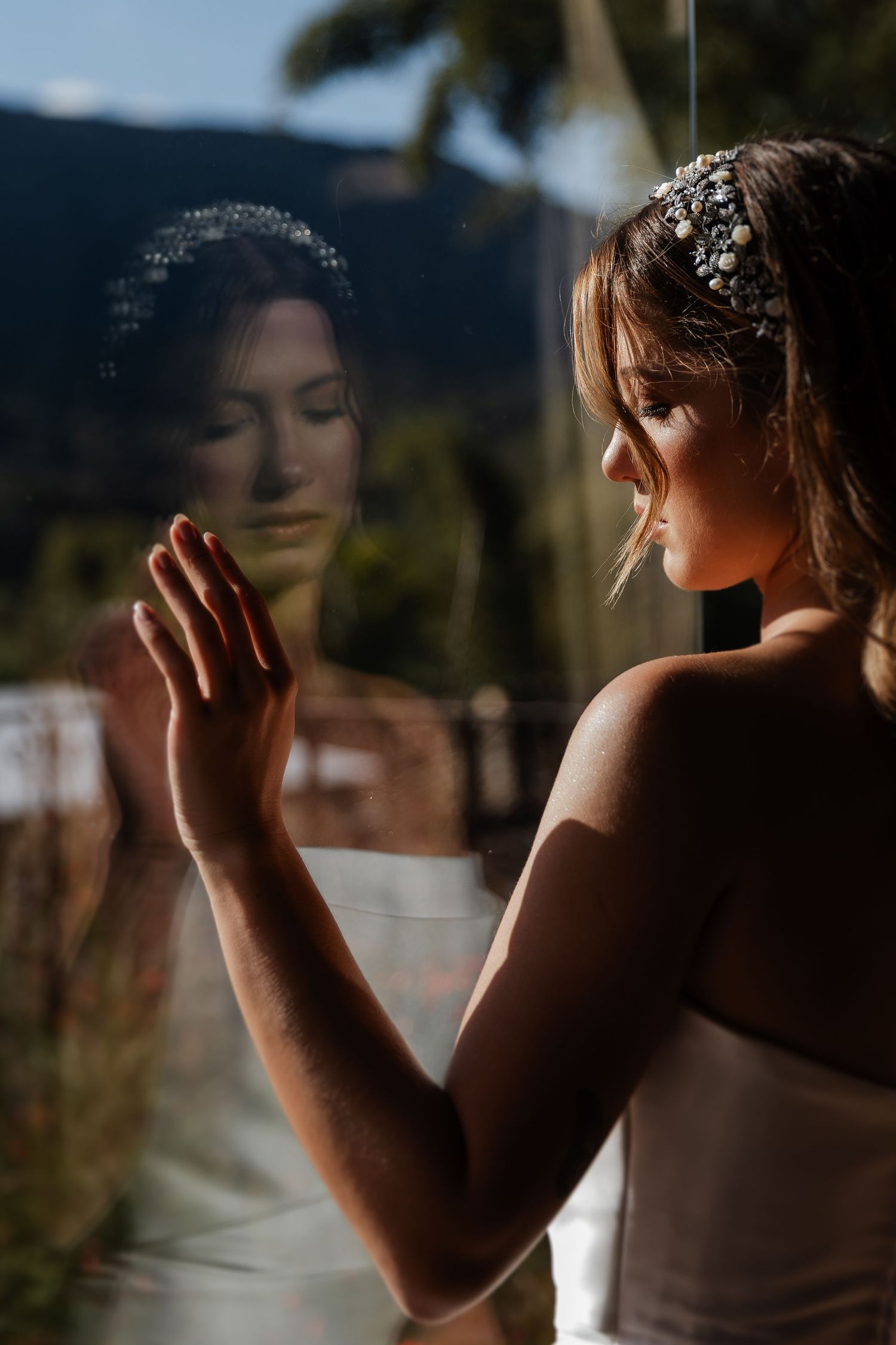 A person in a white dress touches a window glass pane creating a soft reflection in warm golden light.