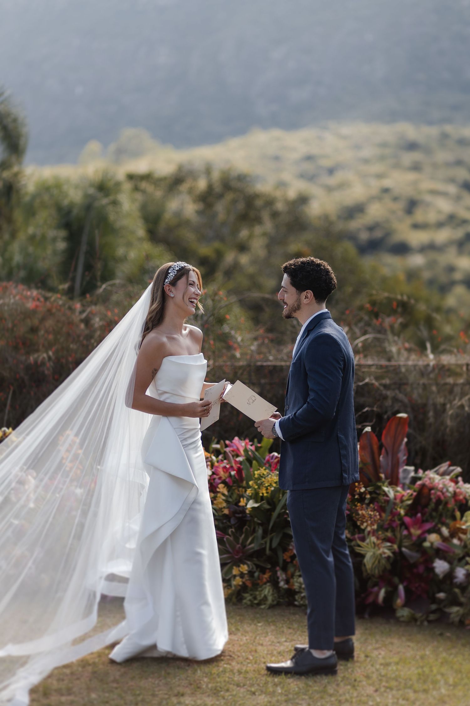 Outdoor wedding ceremony shows couple exchanging vows on hilltop surrounded by colorful flowers.