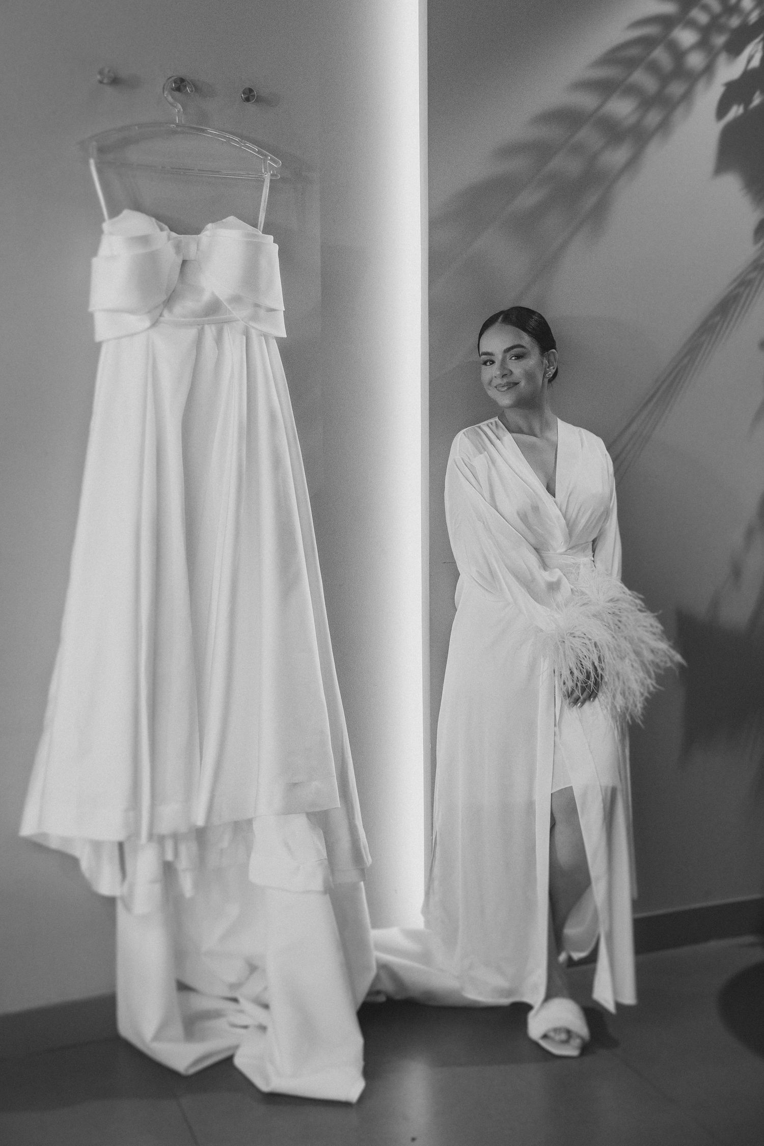 casamento em Belo Horizonte, Black and white wedding photograph showing a hanging bridal gown and figure in white robe with feather details.