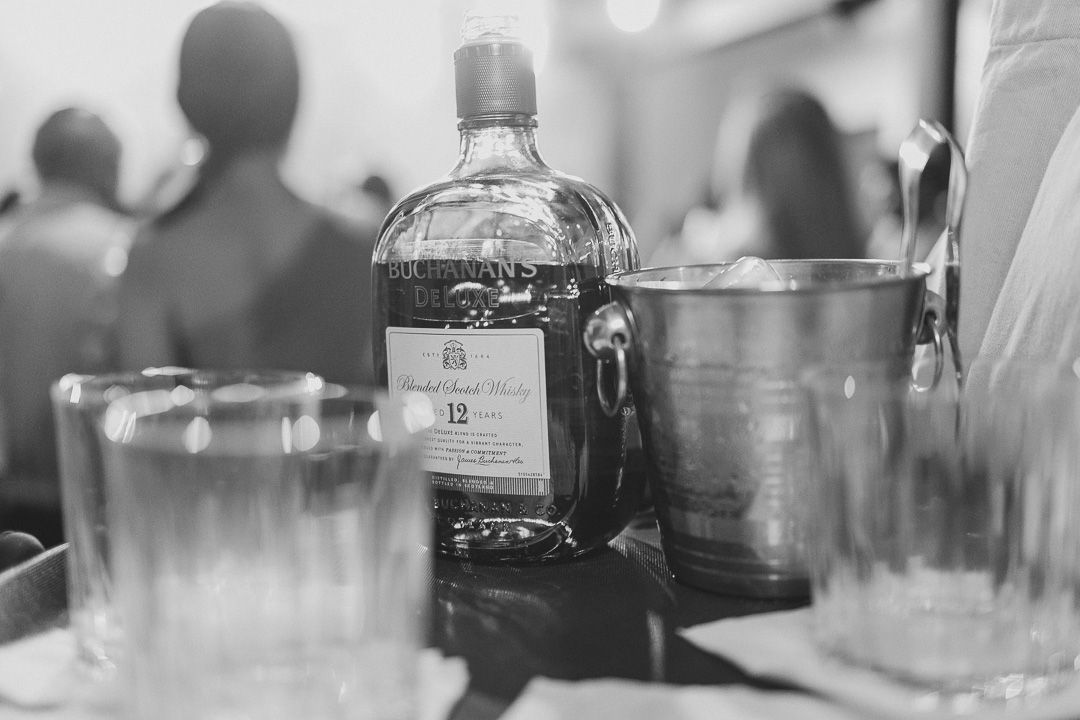 Black and white photo of a whiskey bottle on a table with empty drinking glasses in a bar setting.