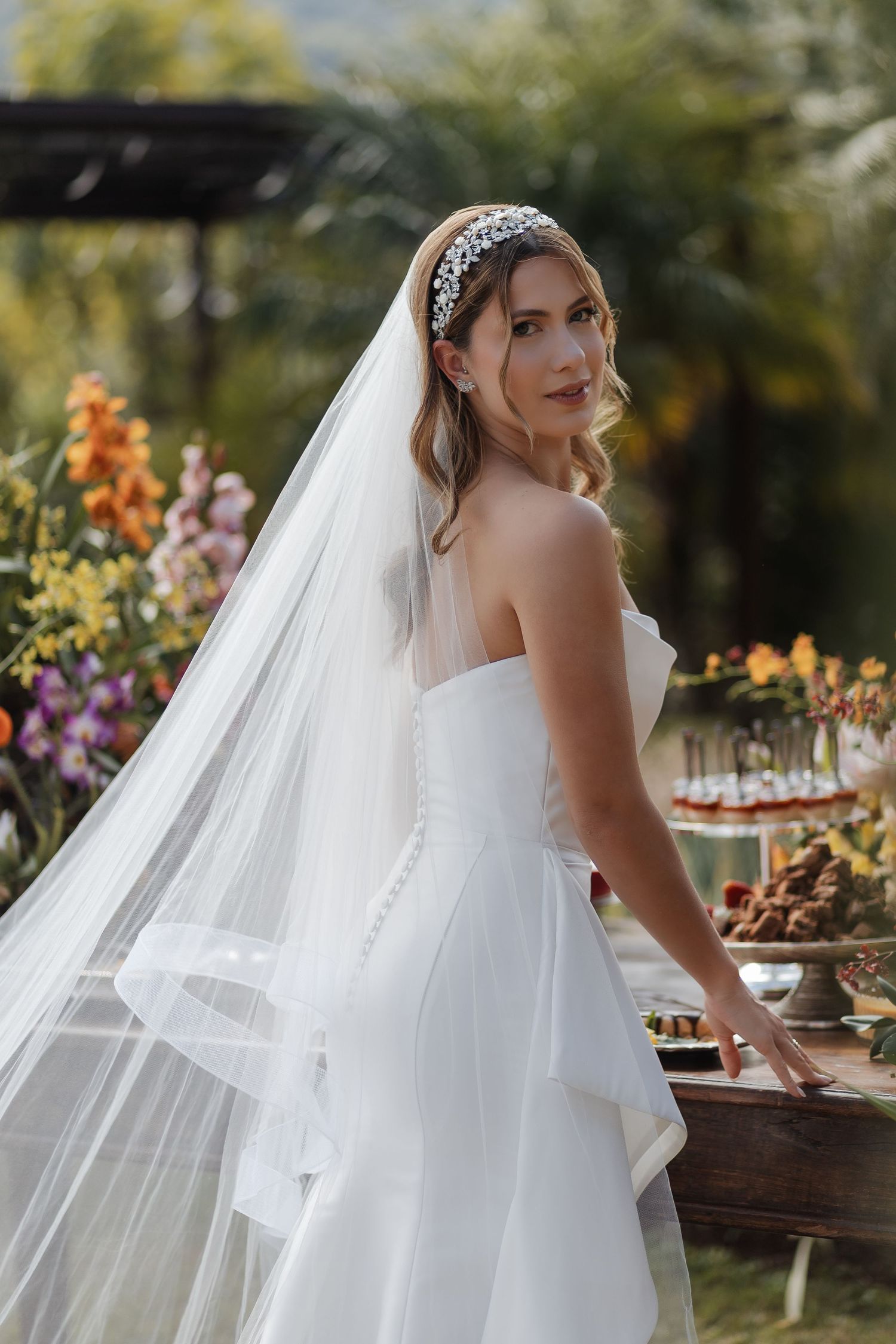 A bride in a white veil and dress at an outdoor garden wedding reception with floral centerpieces and table decor.