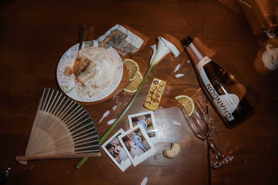 Wooden table with vintage fan, polaroid photos, cocktail glasses, and drink bottles in moody lighting.