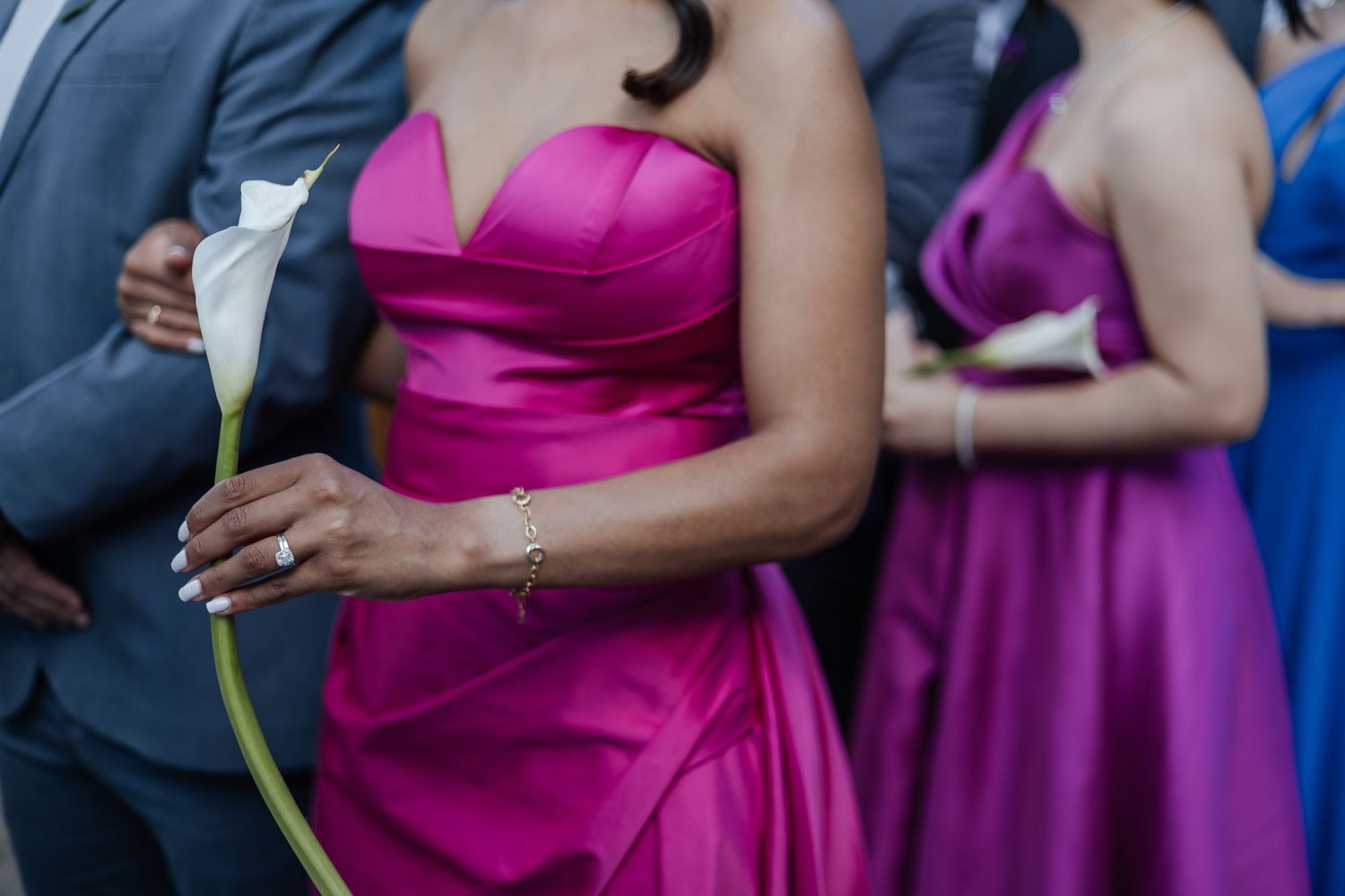 A group of wedding attendants wearing vibrant pink and purple dresses stand together holding yellow flowers.