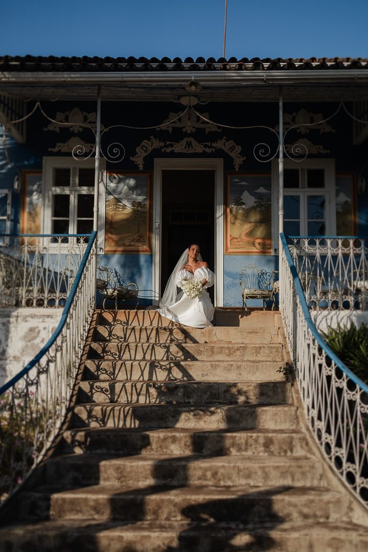 A vintage blue colonial house with ornate railings and steps showcases elegant architectural details against a bright sky.
