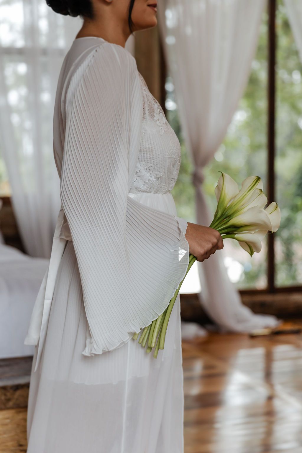Fotógrafo de casamento em SP, AlA white wedding dress with ribbed bell sleeves and lace details shown from the side with calla lily bouquet.