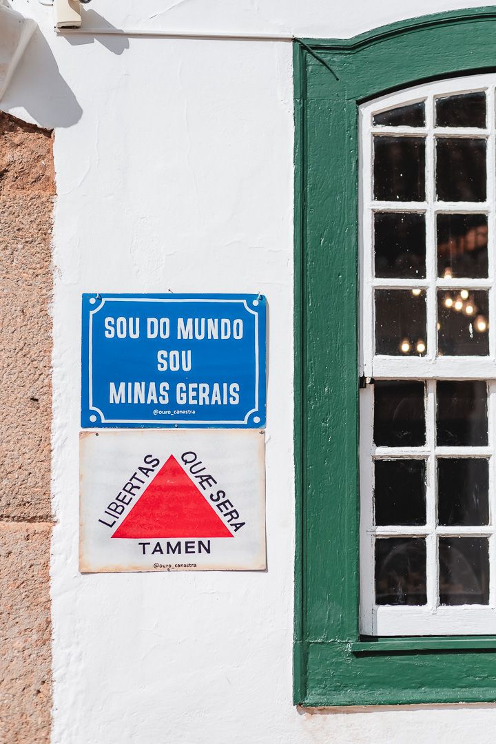 Brazilian street sign reading 'SOU DO MUNDO SOU MINAS GERAIS' with Minas Gerais state motto next to green window frame.