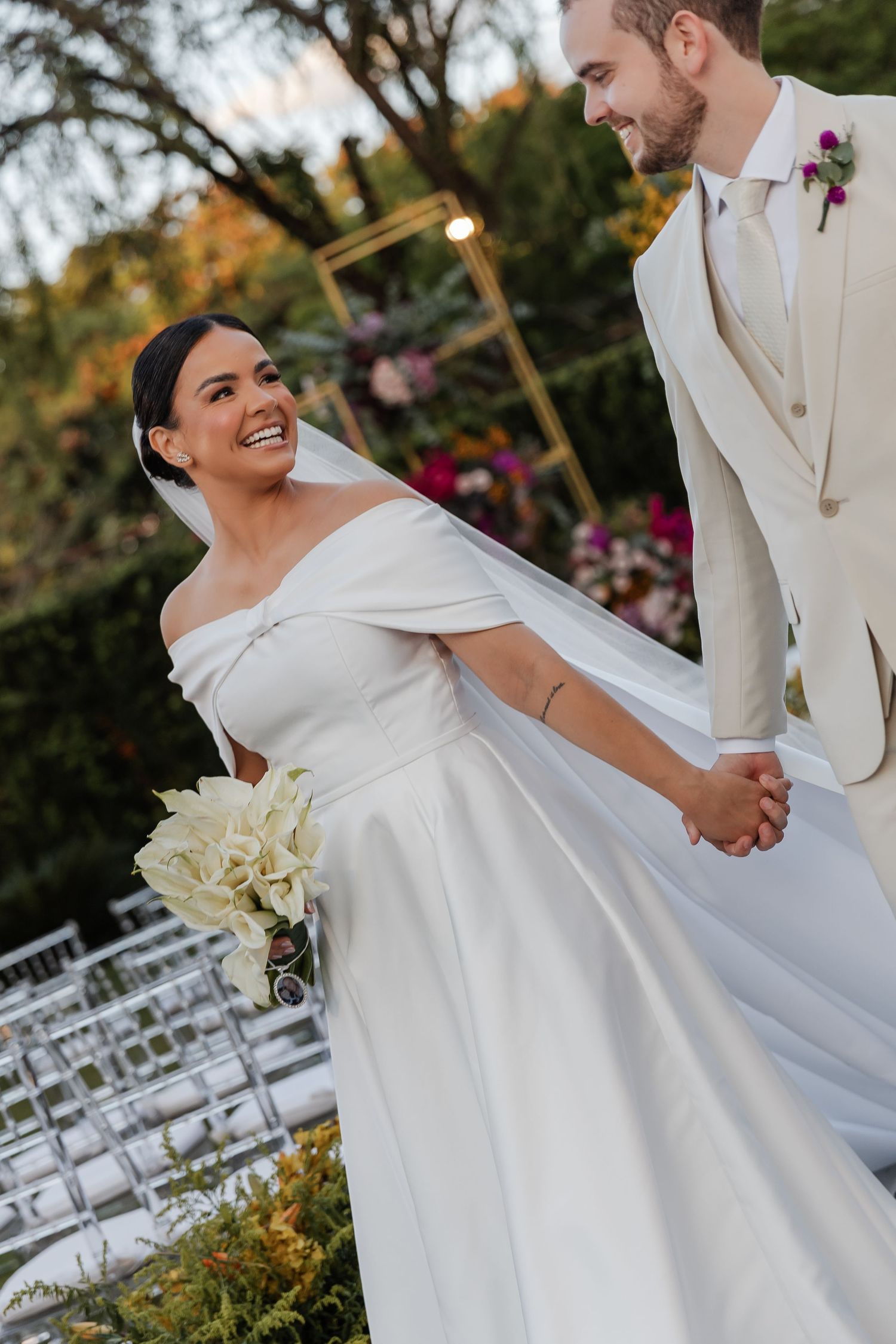 A bride and groom share a joyful moment during their outdoor garden wedding ceremony with white chairs in the background.