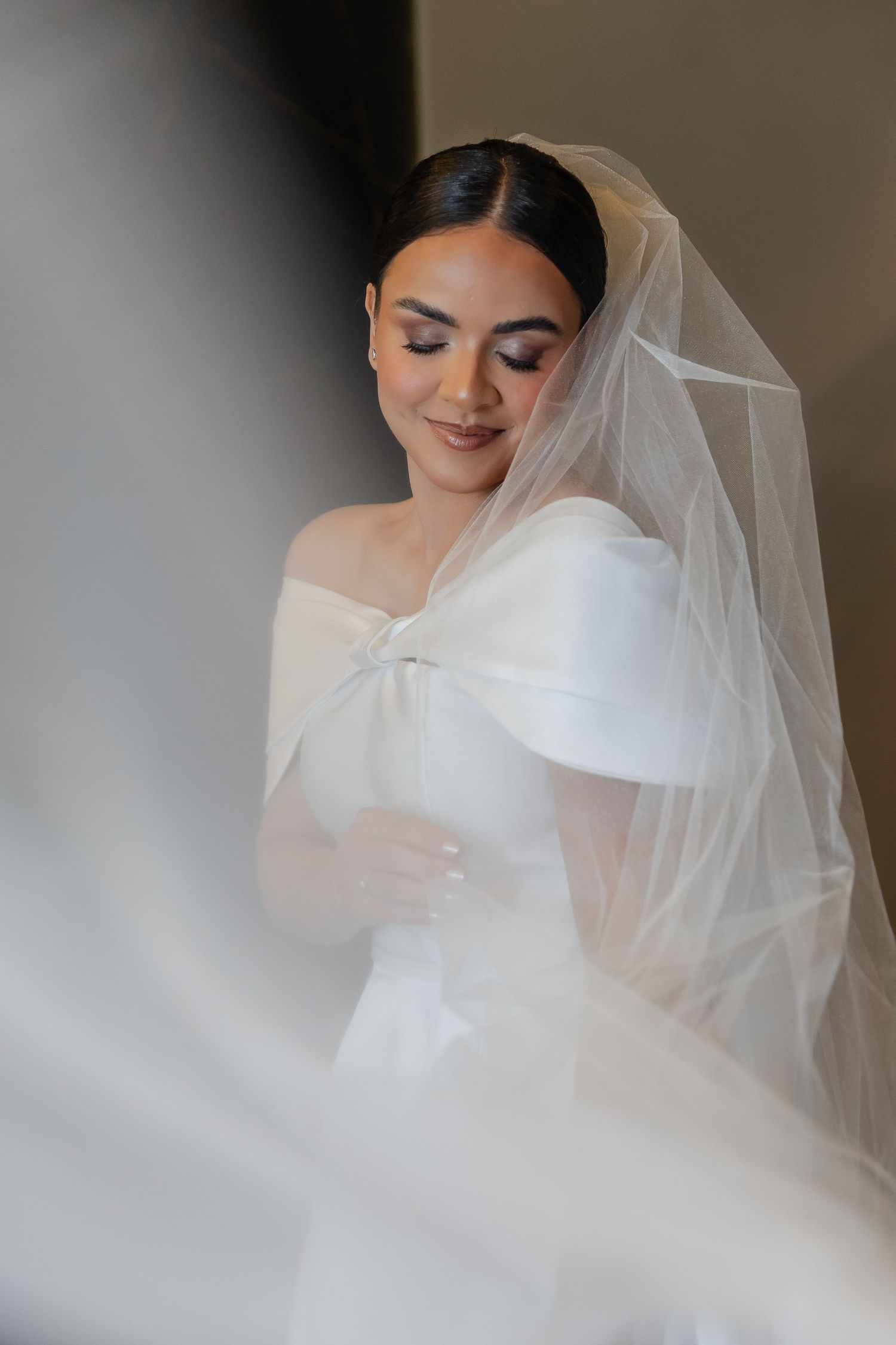 A bride in a romantic white veil and dress poses for ethereal wedding portraits with soft lighting and gentle movement.