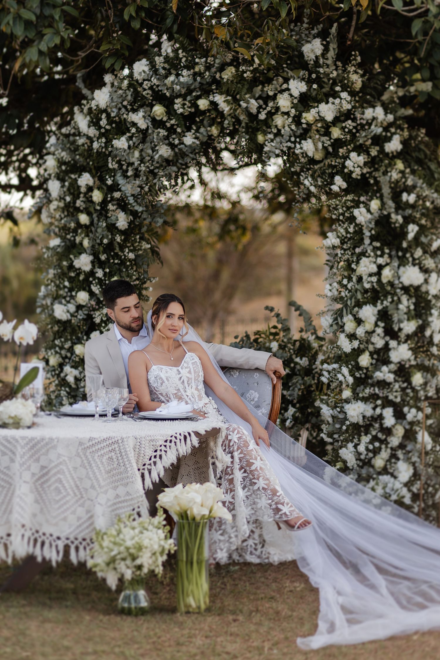 A romantic outdoor wedding scene with floral arches and white decor creates an elegant garden atmosphere.