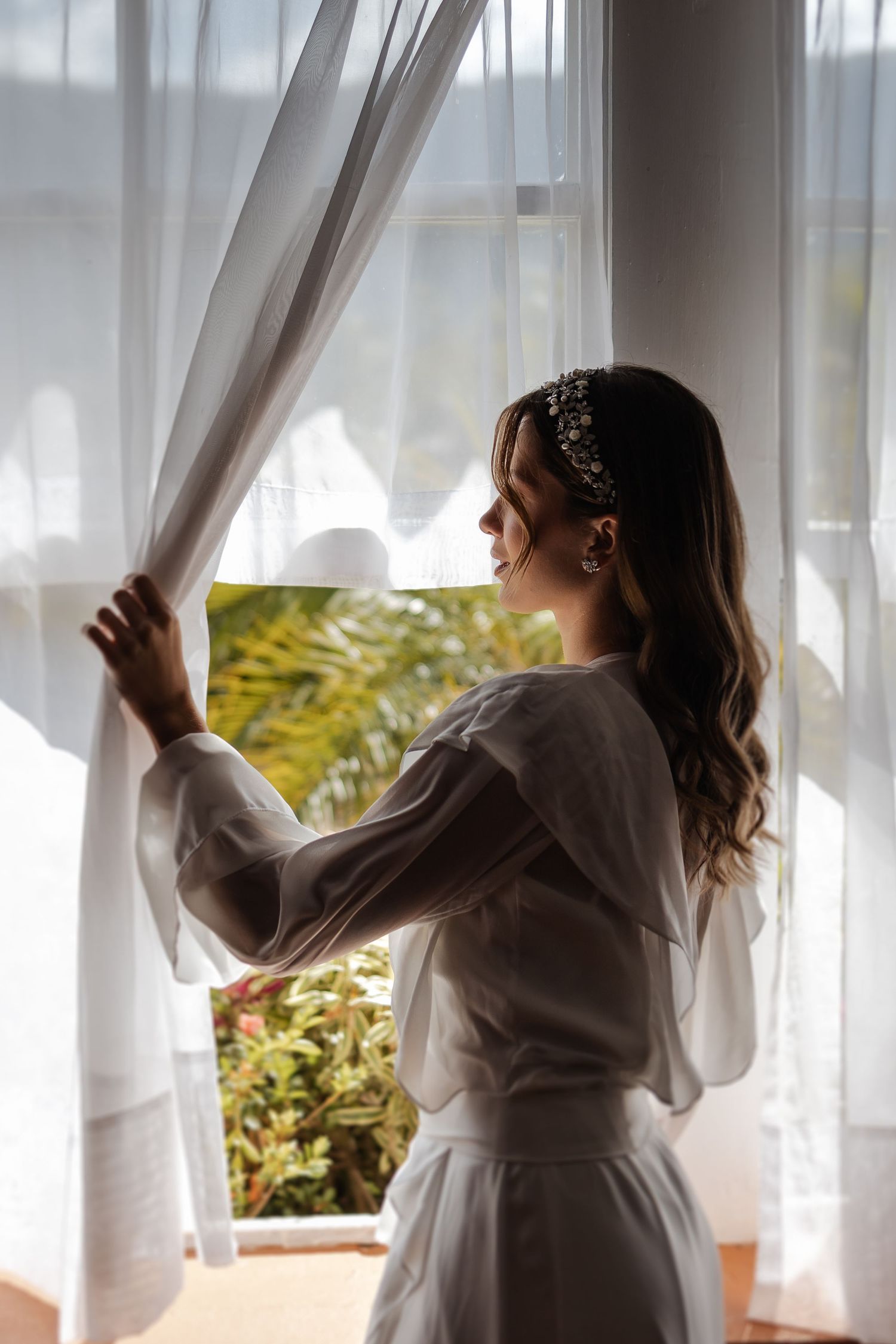 Four views of woman in white dress opening flowing sheer curtains in sunlit room with green plants outside.