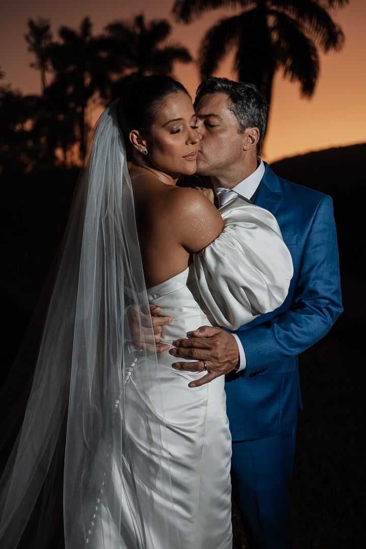 Romantic wedding photo of bride and groom sharing an intimate moment at sunset with palm trees in the background.