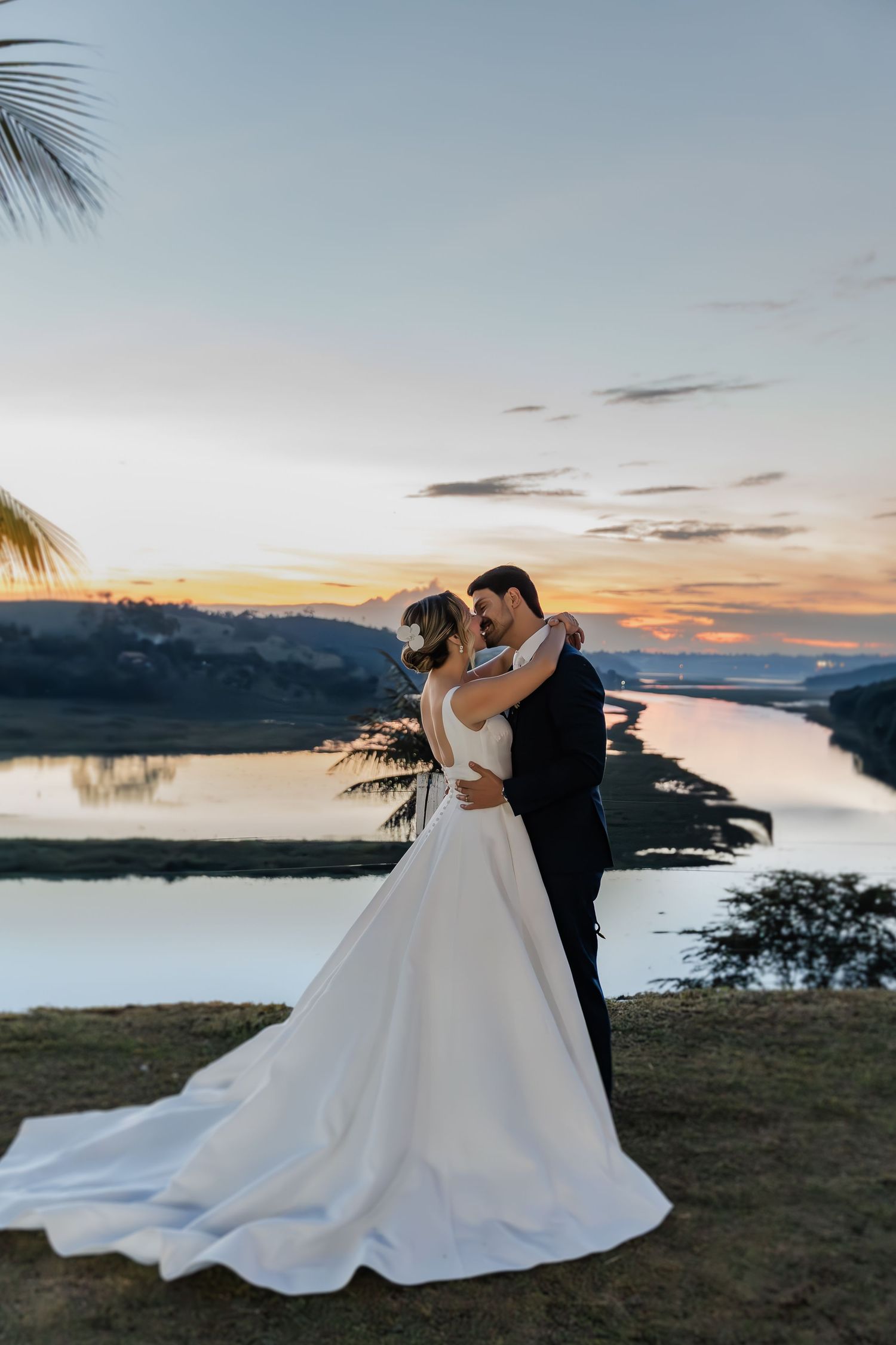 A romantic sunset wedding portrait overlooking a serene lake and mountains with palm trees framing the scene.