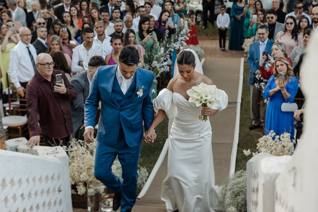 Happy couple walking down white aisle lined with baby's breath flowers after wedding ceremony as guests celebrate.