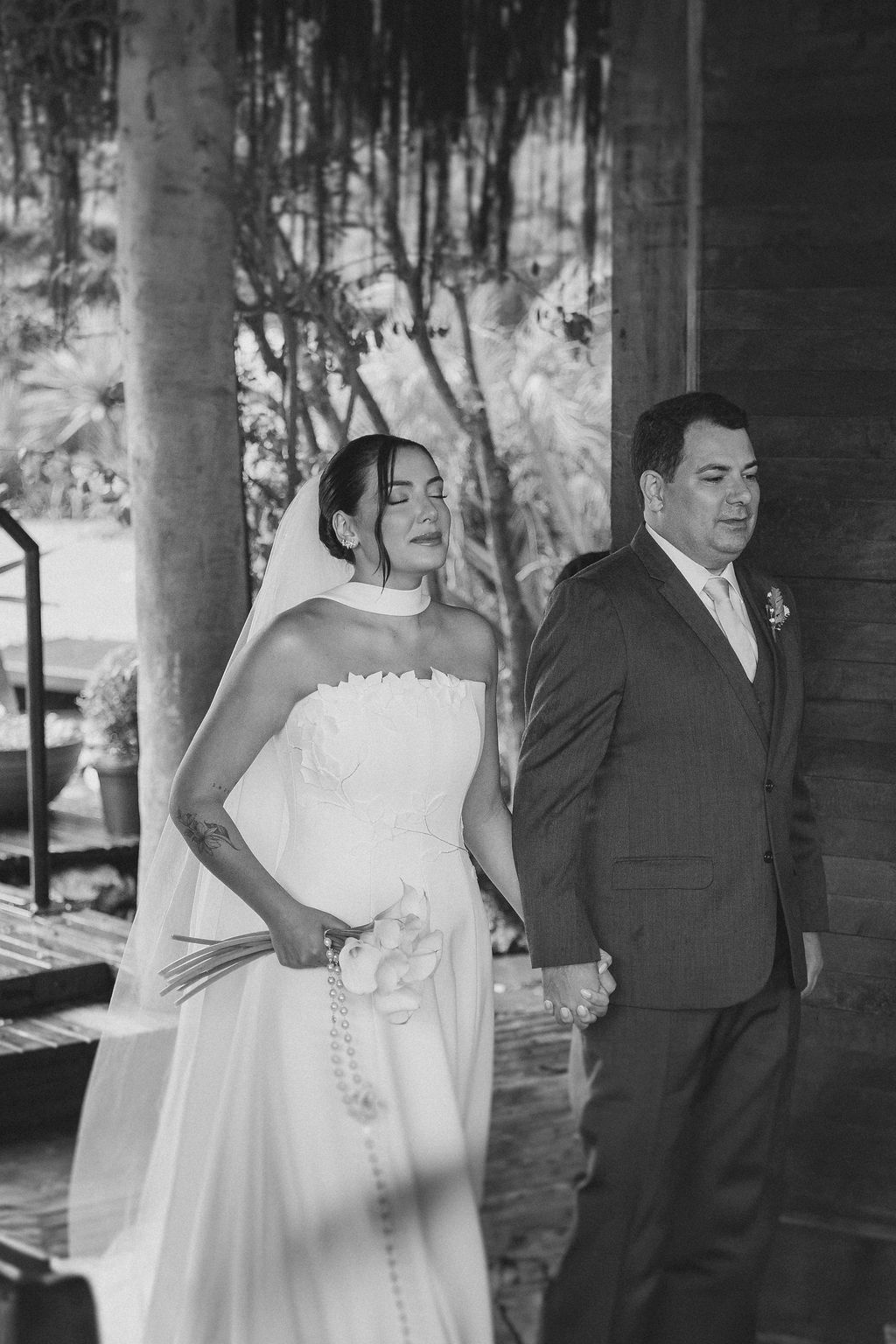 A black and white wedding portrait of a couple in formal attire standing together under an outdoor pavilion.