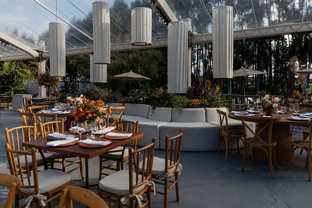 Outdoor restaurant patio setup with wooden chairs and tables under modern white pillars at sunset.