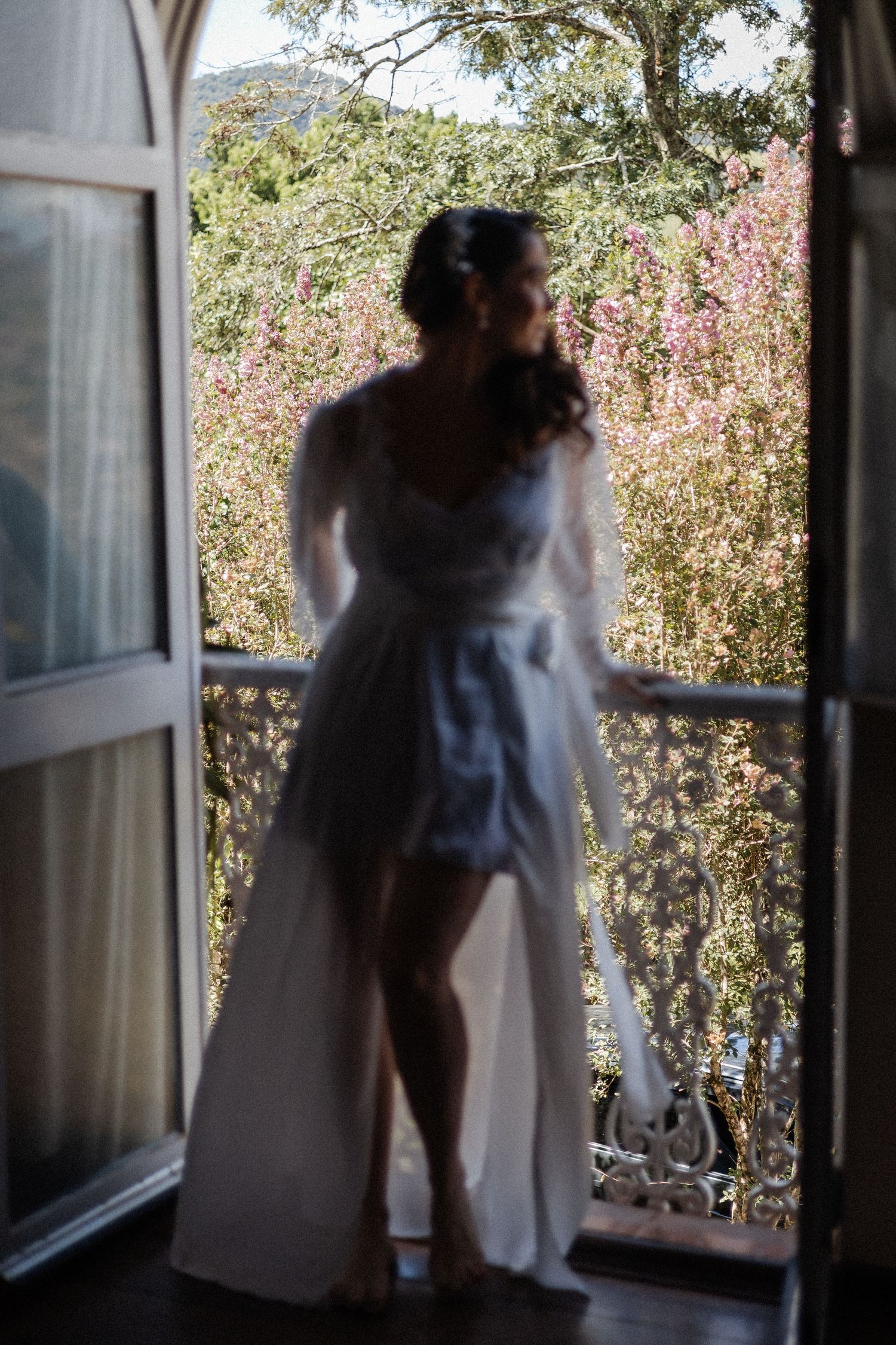 A sequence of silhouettes against a window with trees and pink flowers visible in the background.