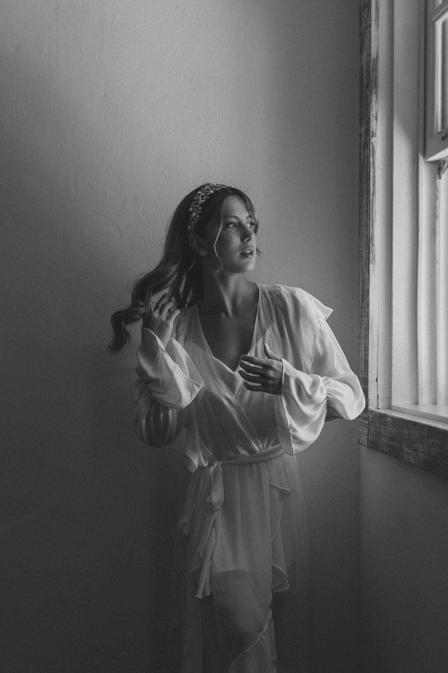 A series of five black and white photos showing a woman in a white robe gazing through a window in different poses.