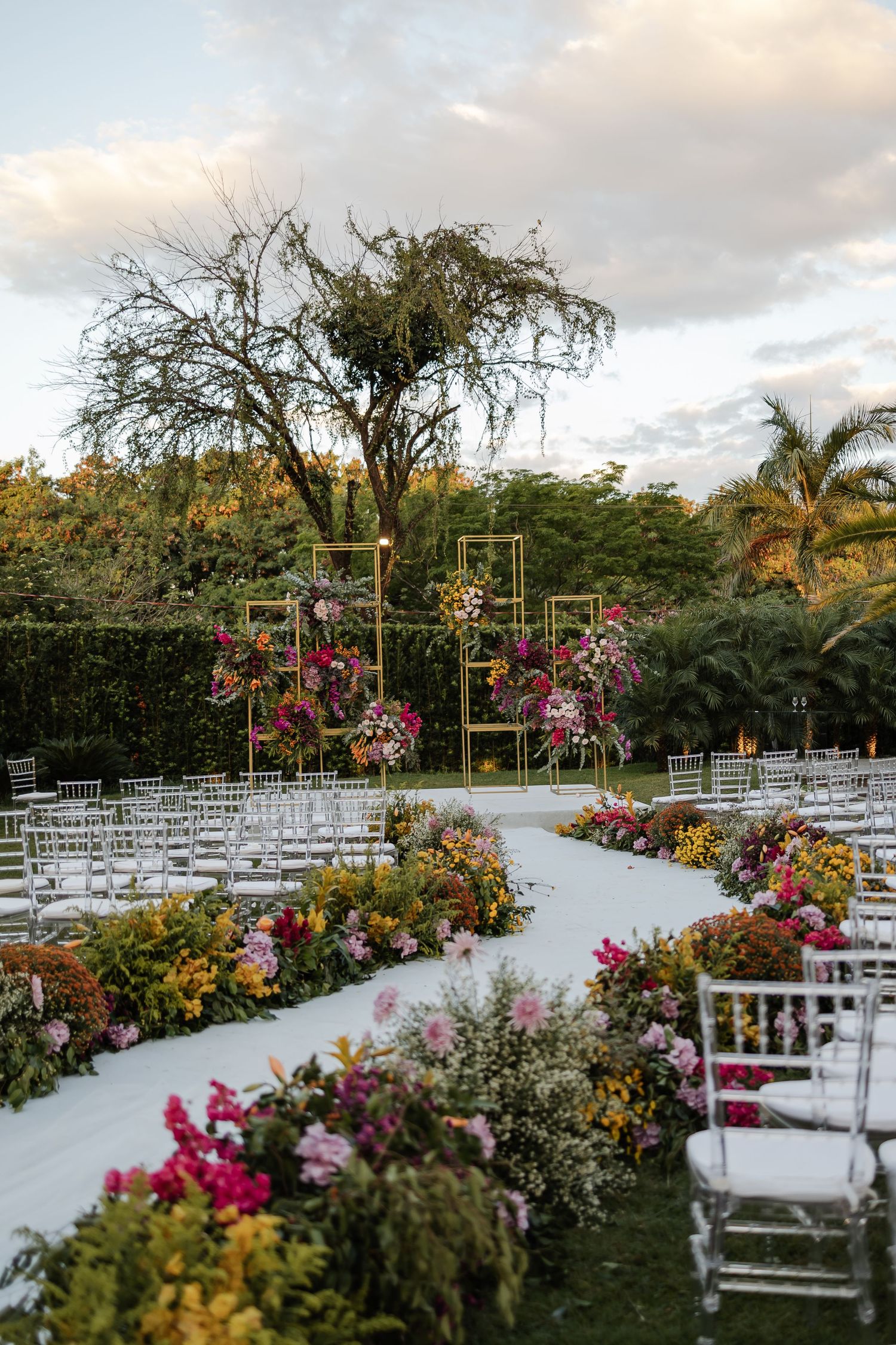casamento em Belo HorizontElegant outdoor wedding ceremony setup with white chairs and vibrant pink floral arrangements along a white aisle.