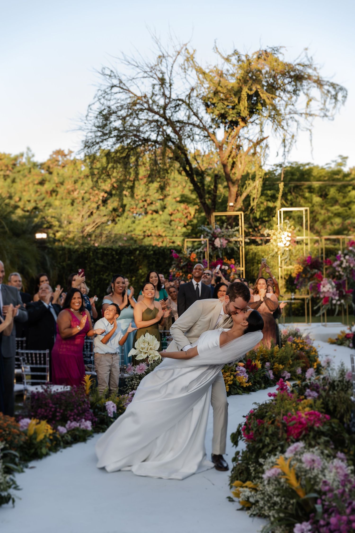 A romantic outdoor wedding ceremony with couples dancing surrounded by colorful flowers and garden scenery at sunset.