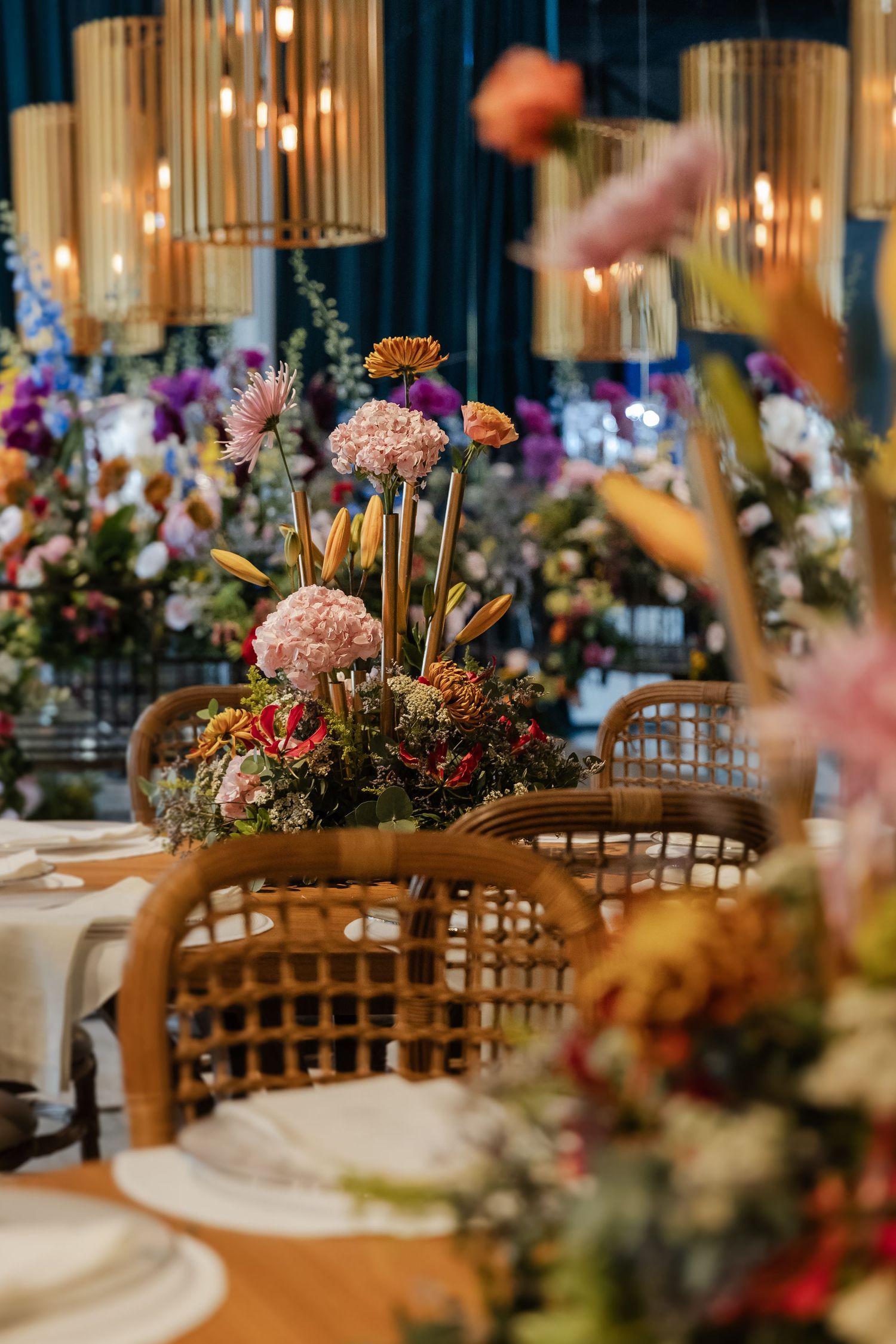 Elegant table settings with wooden chairs and colorful floral centerpieces at an indoor banquet or wedding reception.