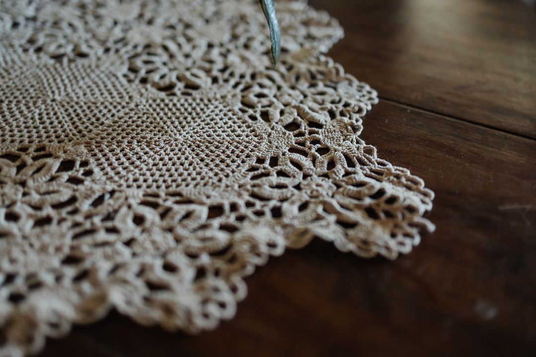 Foto do casal na Fazenda Pedra Negra, Close up view of white lace doily with intricate crochet pattern details on dark wooden table surface.