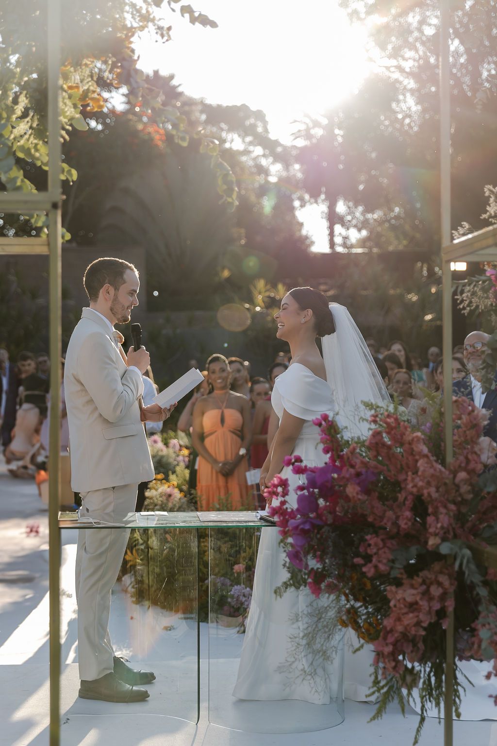 A couple exchanges vows during an outdoor wedding ceremony with beautiful pink floral arrangements in golden sunlight.